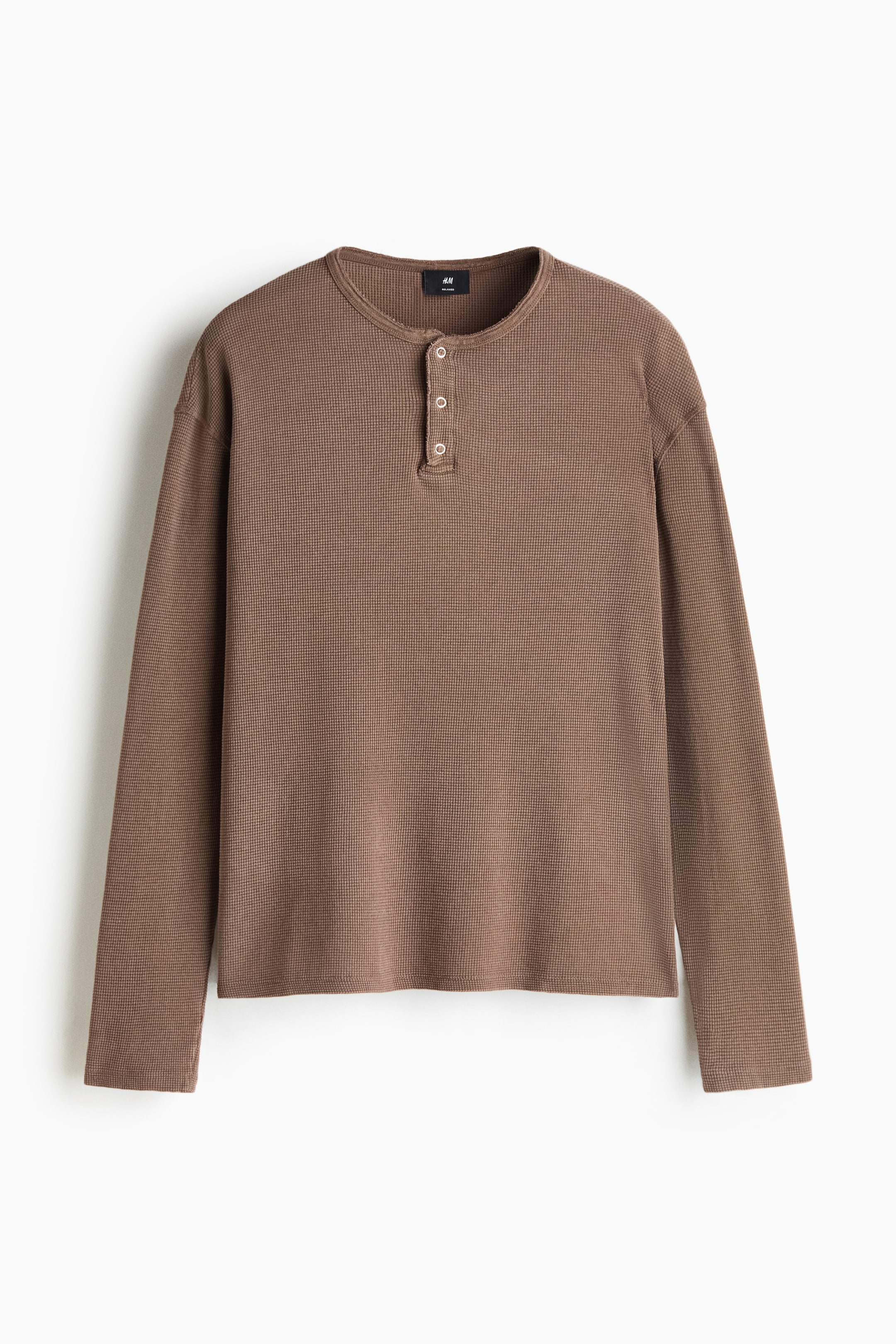 Agrandir l'image: Un haut Henley marron à manches longues en jersey de coton gaufré est présenté de face, avec une coupe décontractée et des épaules tombantes. Le haut affiche un col rond avec une patte de boutonnage à trois boutons, des poignets droits simples et un ourlet droit.
