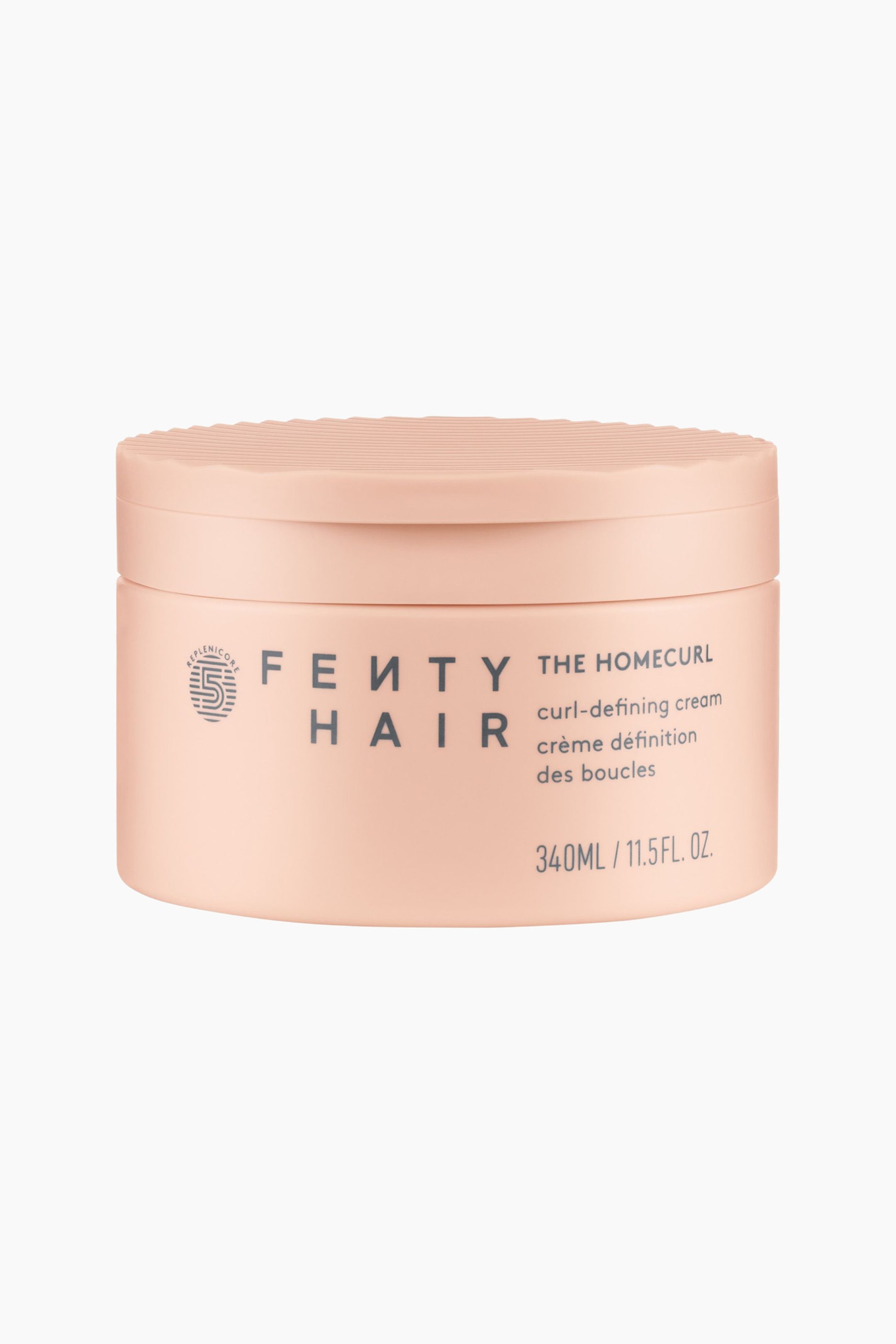 Visa större bild: Homecurl Curl-defining Cream står upprätt och visar upp sin cylindriska burk i persikofärgad ton med ett matchande texturerat, räfflat lock. Den framåtvända burken visar logotypen ”Fenty Hair”, ett cirkelformat emblem, produktnamnet ”The Homecurl” samt volymuppgifter i mörkgrå text.