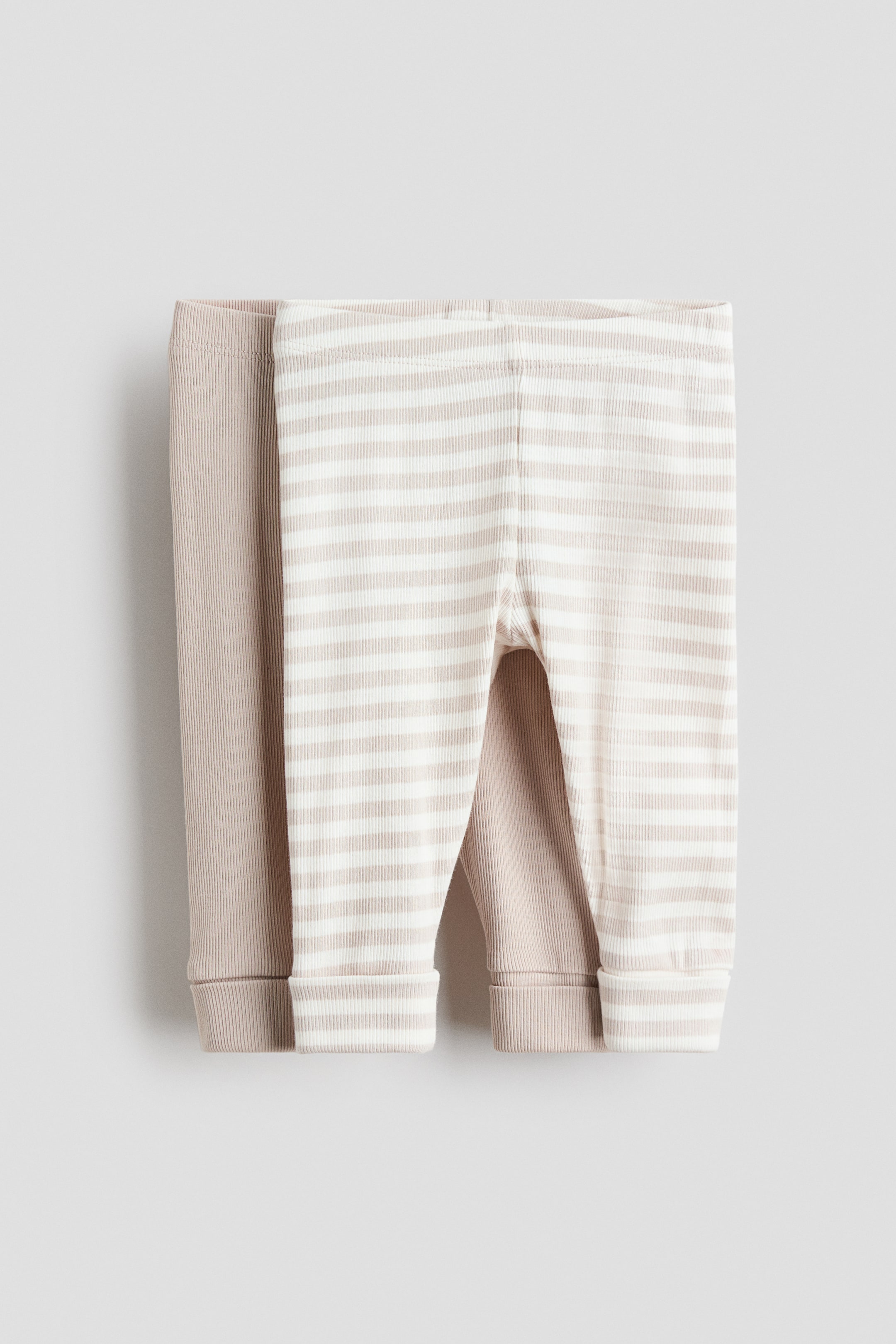 Visa större bild: Leggingsna visas från framsidan, med två par gjorda av ribbad bomullsjersey. Ett par är i en enfärgad beige färg och det andra har beige och vita ränder; båda visar täckt resår i midjan och manschetter vid fållen.