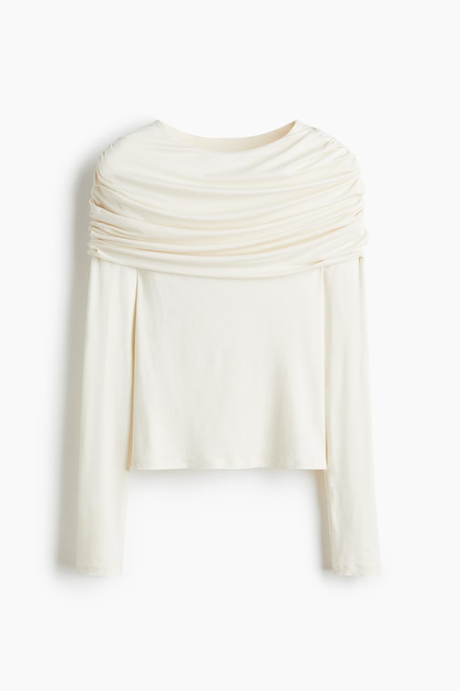 Se presenta una blusa de manga larga en color crema, con un detalle destacado de drapeado y fruncido en el pecho y los hombros, con un escote redondo y un dobladillo recto. - 1