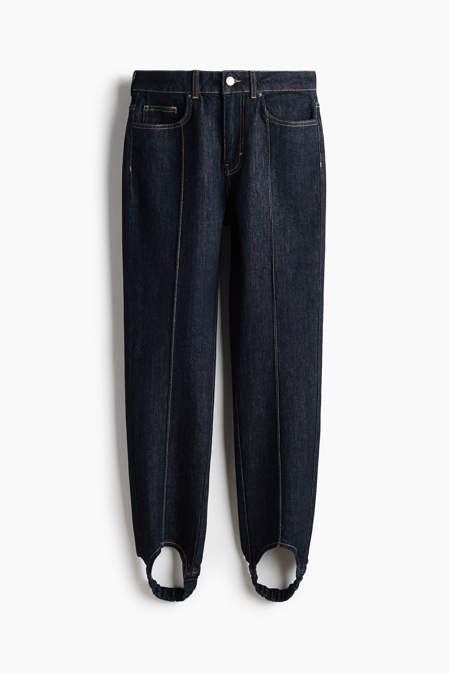 Para ciemnoniebieskich jeansÃ³w z denimu typu stirrup jest pokazana z przodu, z wysokim stanem i piÄcioma kieszeniami oraz kontrastowymi przeszyciami. Pionowe szwy pintuck biegnÄ wzdÅuÅ¼ Årodka kaÅ¼dej nogawki, zwÄÅ¼ajÄc siÄ ku doÅowi do elastycznych paskÃ³w stirrup przy mankietach. - 1