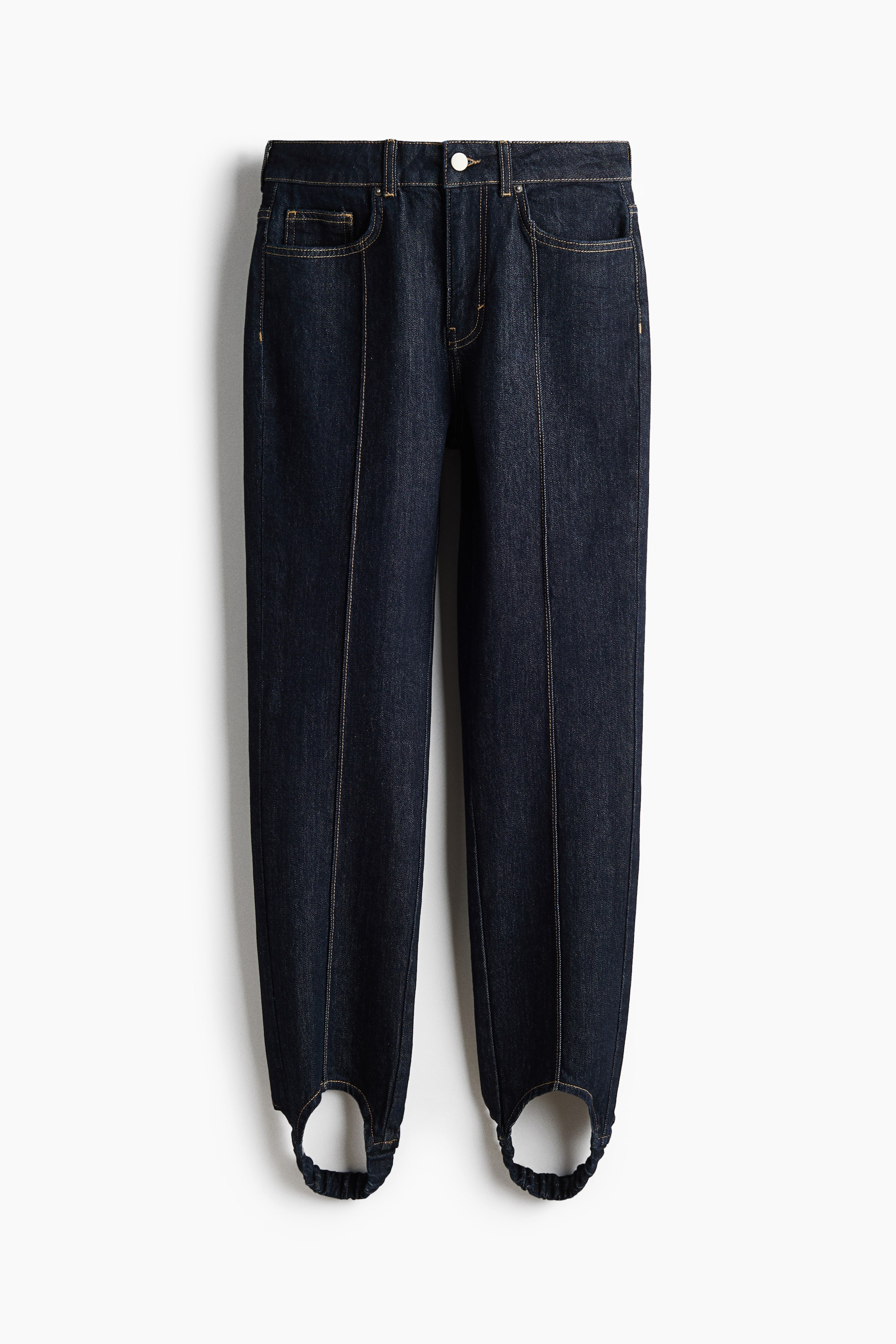 Büyük resmi görüntüle: Koyu yıkamalı mavi denim üzengi paçalı bir kot pantolon çifti önden gösterilmektedir; kontrast üst dikiş detaylarına sahip, yüksek belli ve beş cepli bir tasarıma sahiptir. Her bir paçanın orta hattı boyunca dikey pens dikişleri uzanmakta ve paça uçlarında elastik üzengi bantlarına doğru daralmaktadır.