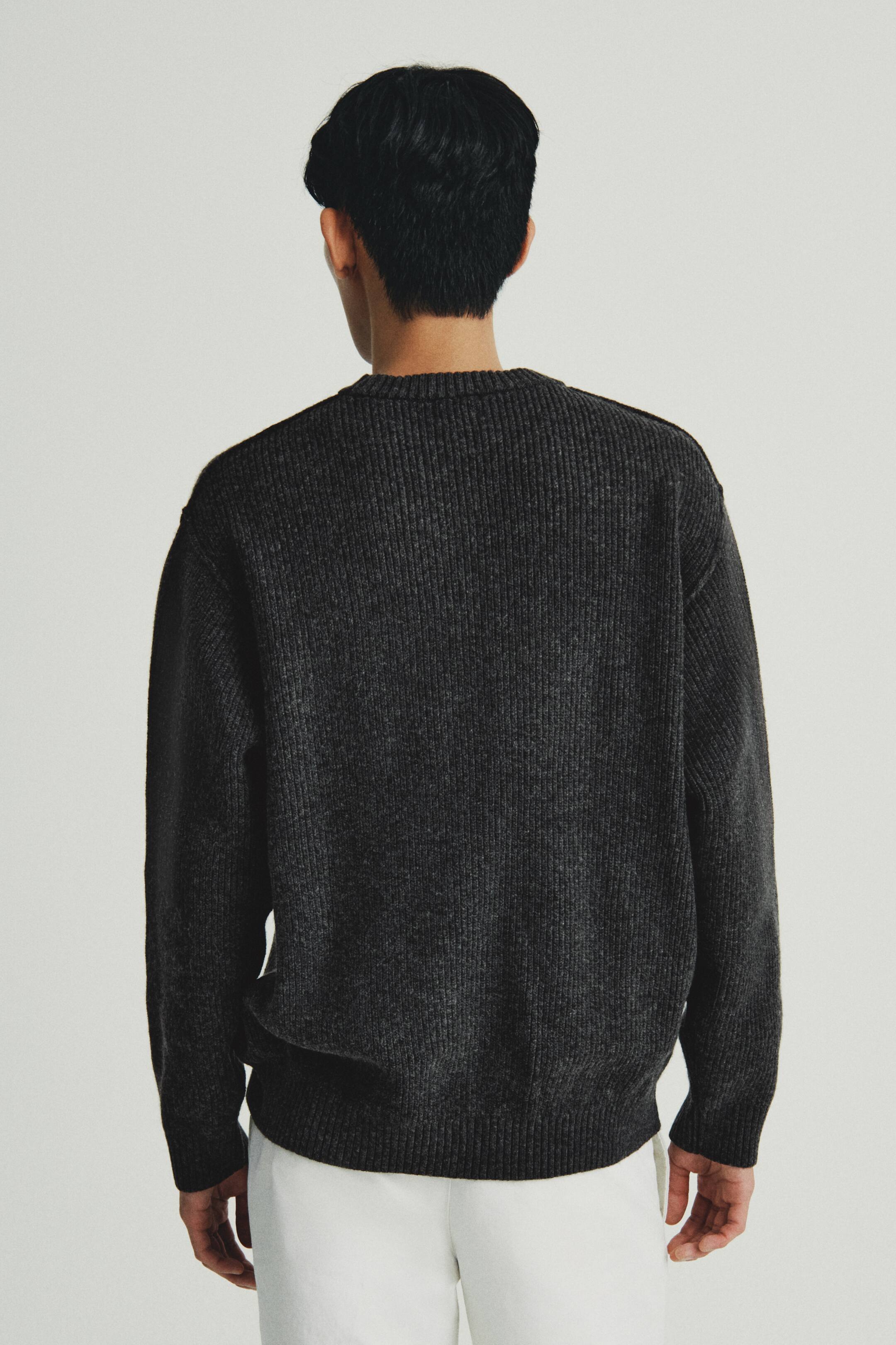 이미지 확대 보기: 어두운 회색 골지 니트 스웨터를 뒷모습으로 입고 있는 모습입니다. 라운드 넥, 골지 소매와 골지 밑단이 있는 긴 소매가 특징입니다.
