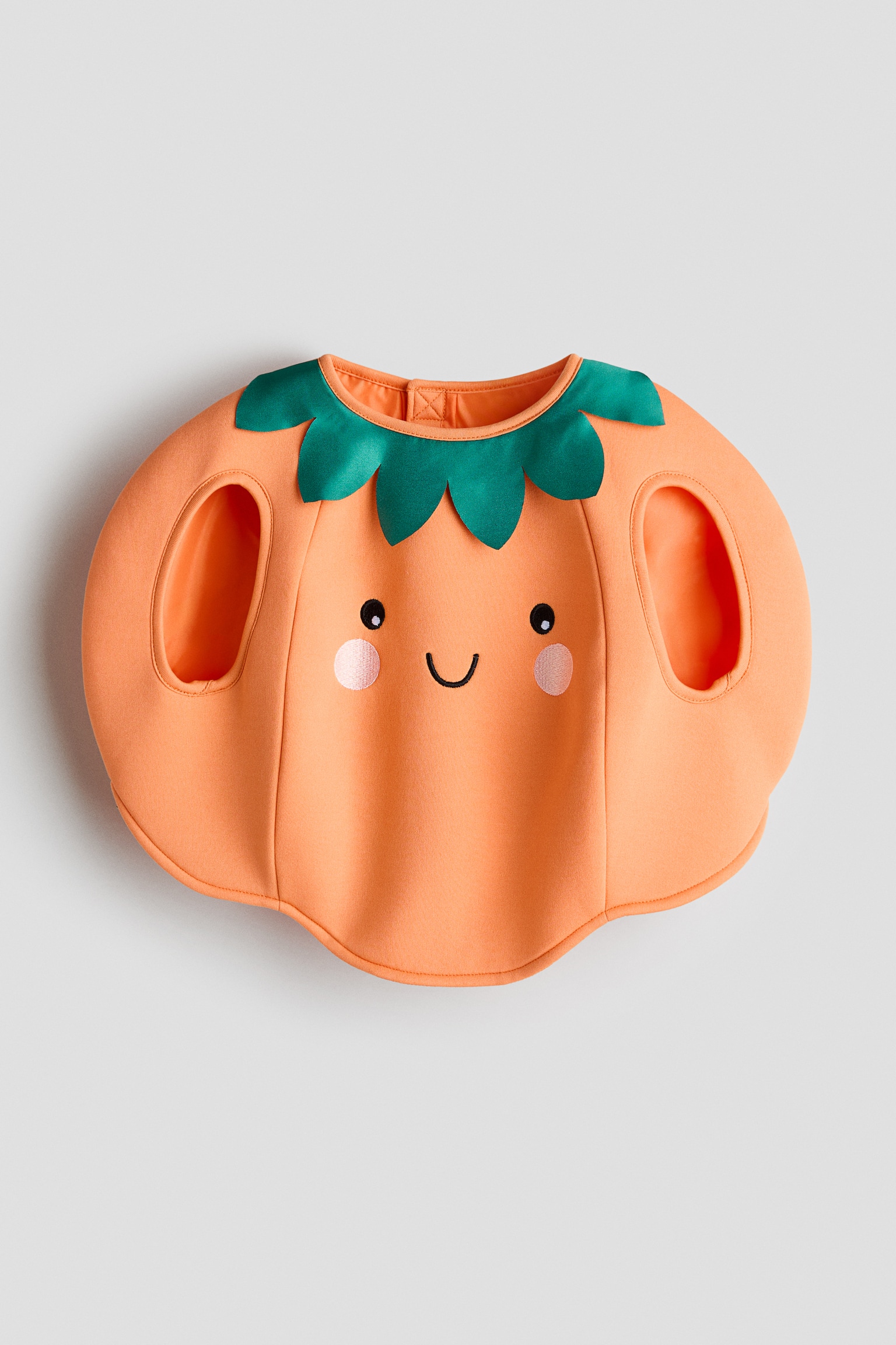 Ein elegantes Kostüm in Form eines orangefarbenen Kürbisses liegt flach und zeigt einen grünen, blattförmigen Kragen um den Halsausschnitt. Auf der Vorderseite sind schwarze, gestickte Augen, ein lächelnder Mund und rosa Wangenkreise zu sehen, mit zwei ovalen Armlöchern an den Seiten. - 1