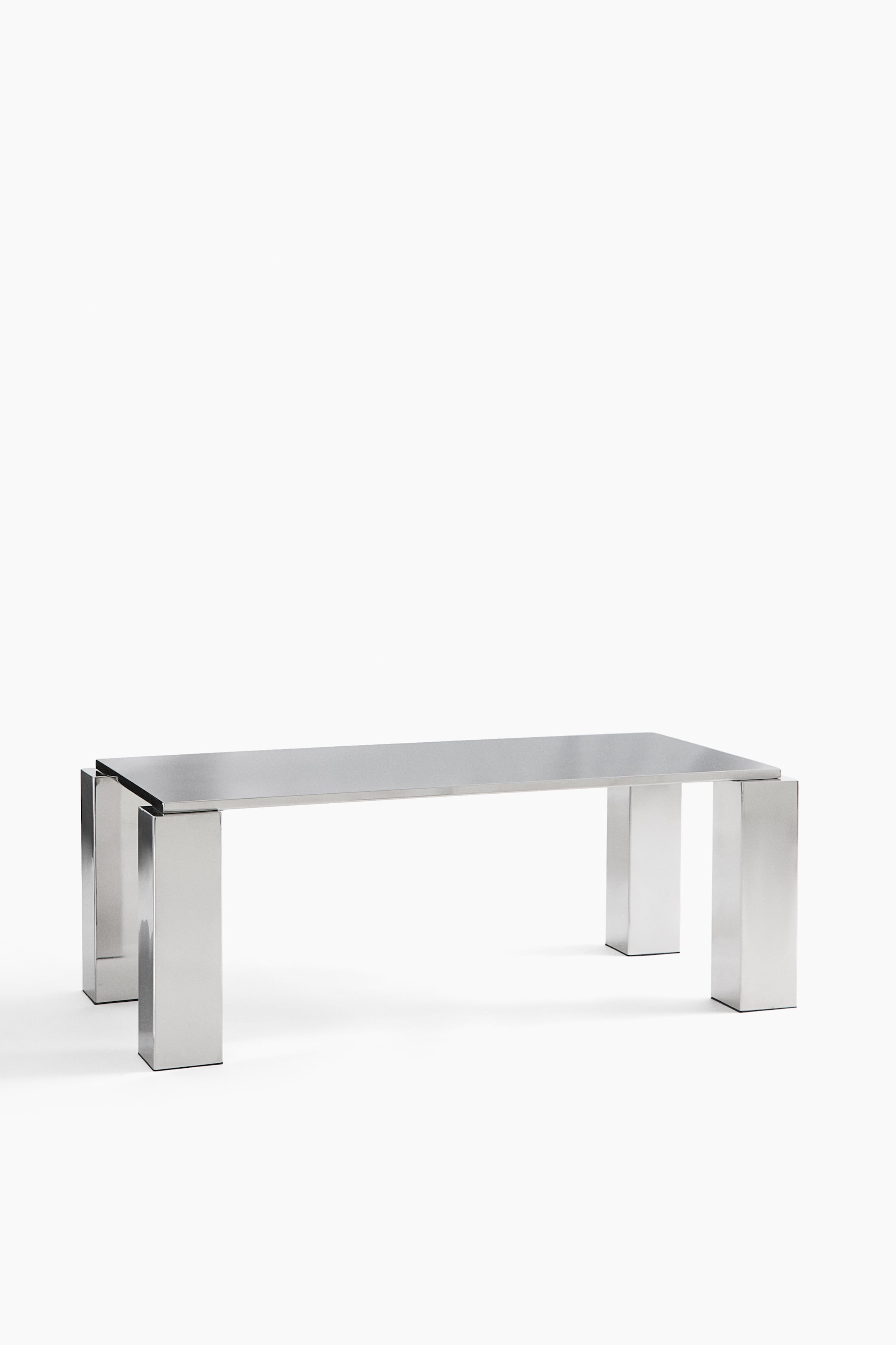 View larger image: A rectangular metal bench is presented in a brushed silver finish. Its rectangular top rests on four rectangular legs, with the outer sections of the legs extending slightly above the top surface.