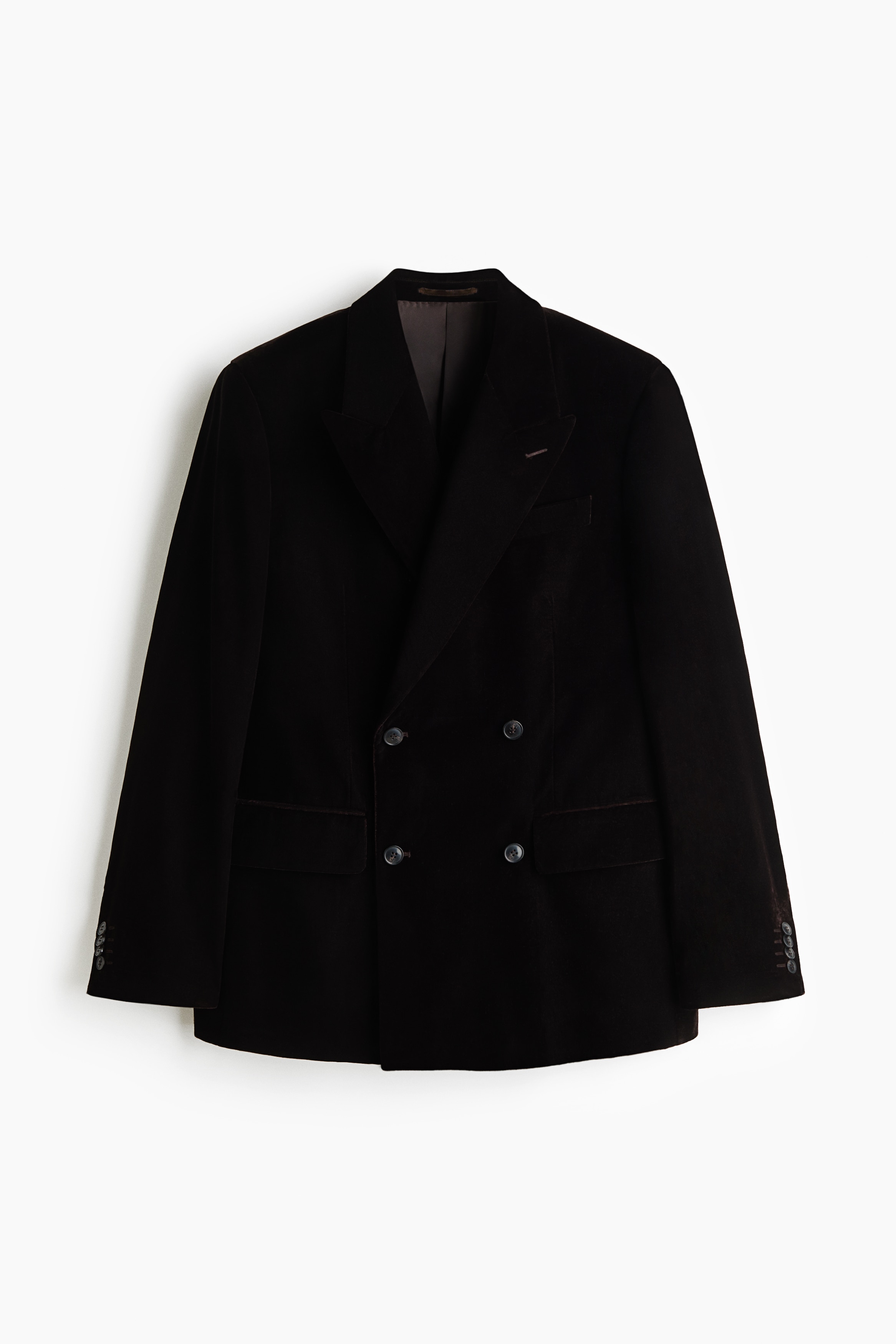 A black velvet double-breasted blazer is shown facing forward, featuring prominent peak lapels, a four-button front closure, and two side flap pockets. The blazer has structured shoulders, a left chest welt pocket, and long sleeves with buttoned cuffs.