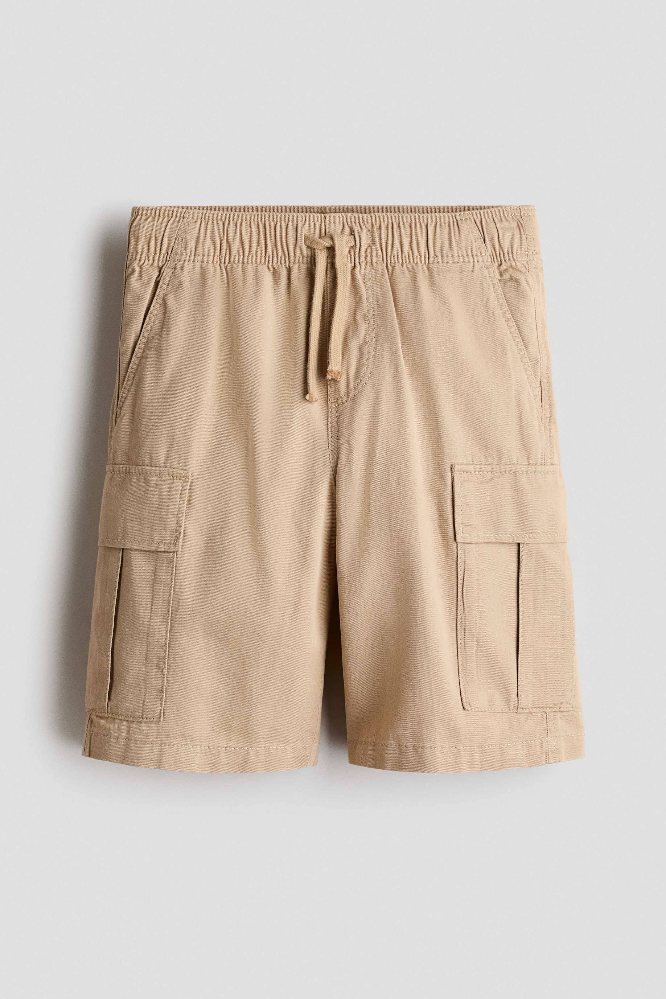 Voir une image plus grande: Une paire de shorts cargo en sergé de coton beige est présentée de face, avec une coupe ample, une taille élastiquée à cordon de serrage et une fausse braguette. Les shorts affichent des poches latérales en biais ainsi que des poches soufflet rectangulaires à rabat sur chaque jambe.