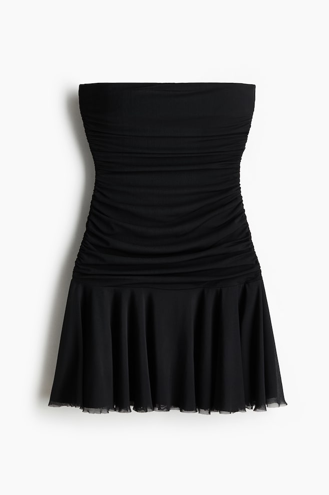 A black strapless dress is showcased from the front. The dress features a ruched bodice that transitions into a flared skirt with a sheer black layer visible at the hem. - 1