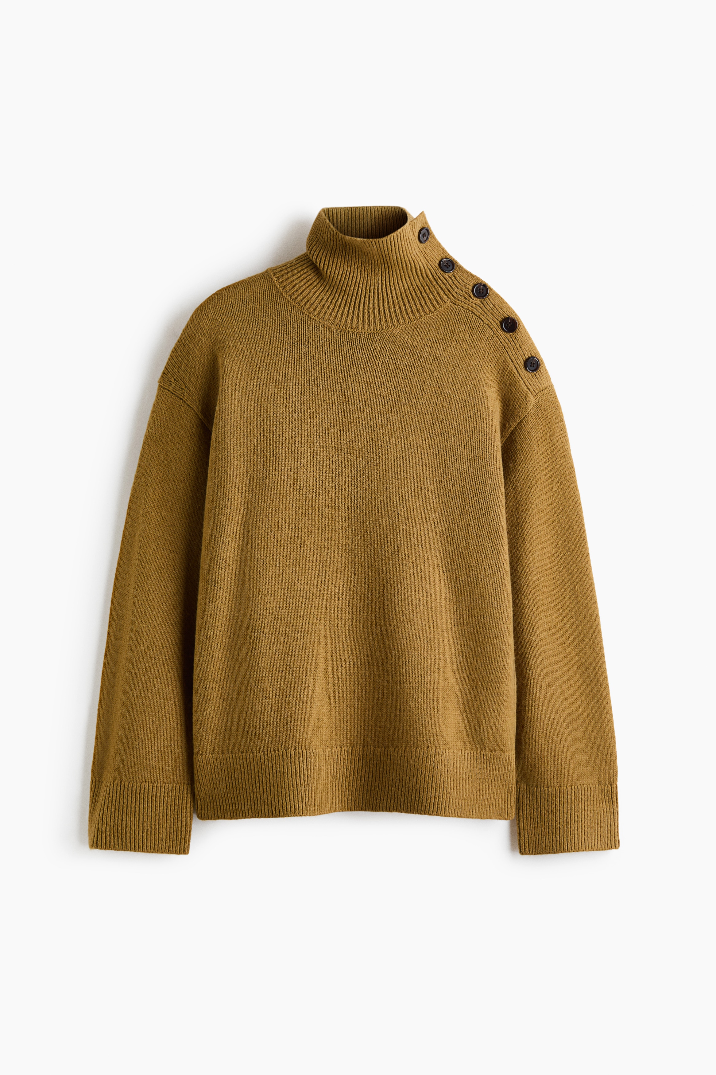 A mustard-yellow knit sweater is being worn by the model, featuring a ribbed high neck and a row of decorative dark buttons along the left shoulder. The oversized sweater has dropped shoulders and is shown partially tucked into dark pants at the waist.