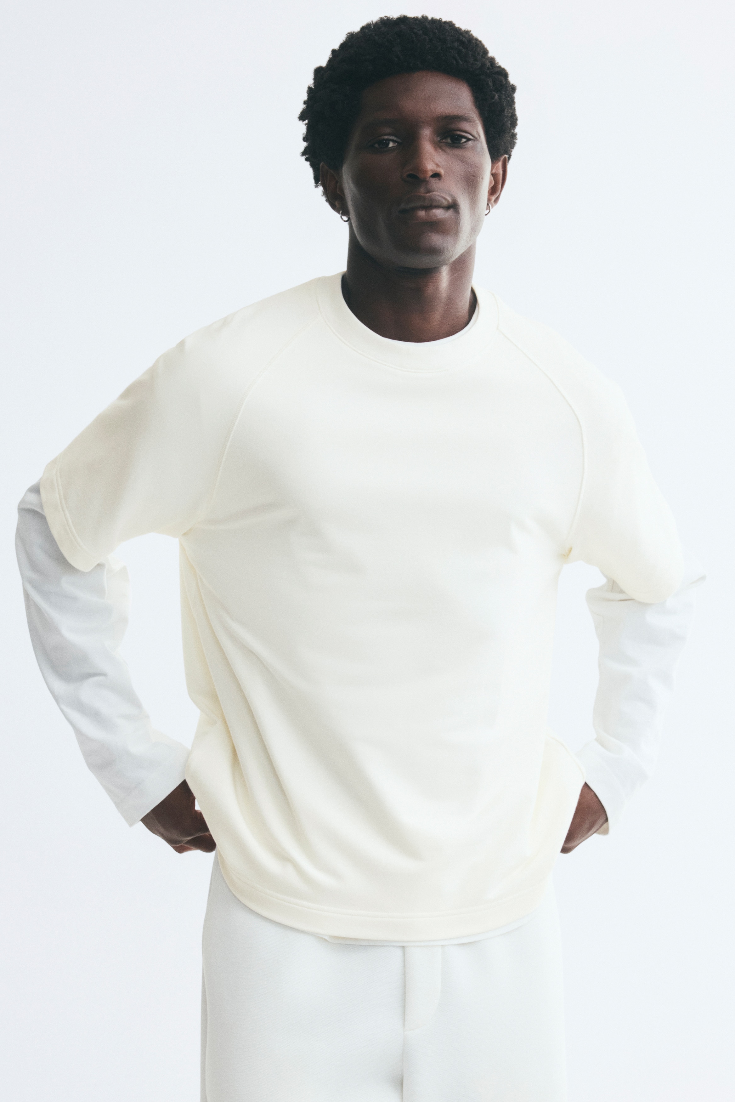 A cream-colored, heavyweight jersey t-shirt is hanging facing front, showcasing a relaxed fit, a round rib-trimmed neckline, short raglan sleeves, and a straight-cut hem.