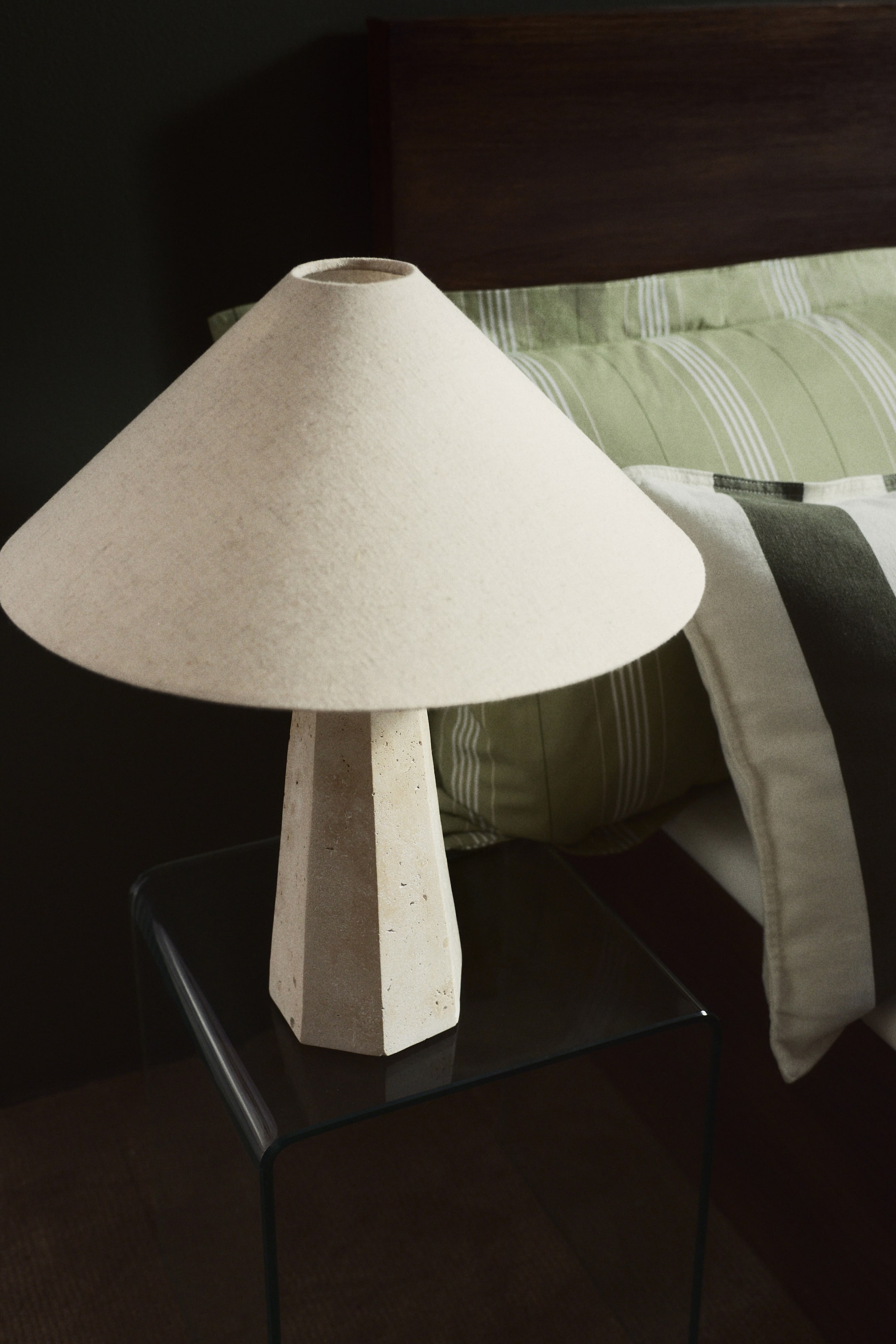 View larger image: A table lamp featuring a light beige conical fabric shade and a tapered, octagonal base made from textured light‑coloured stone.