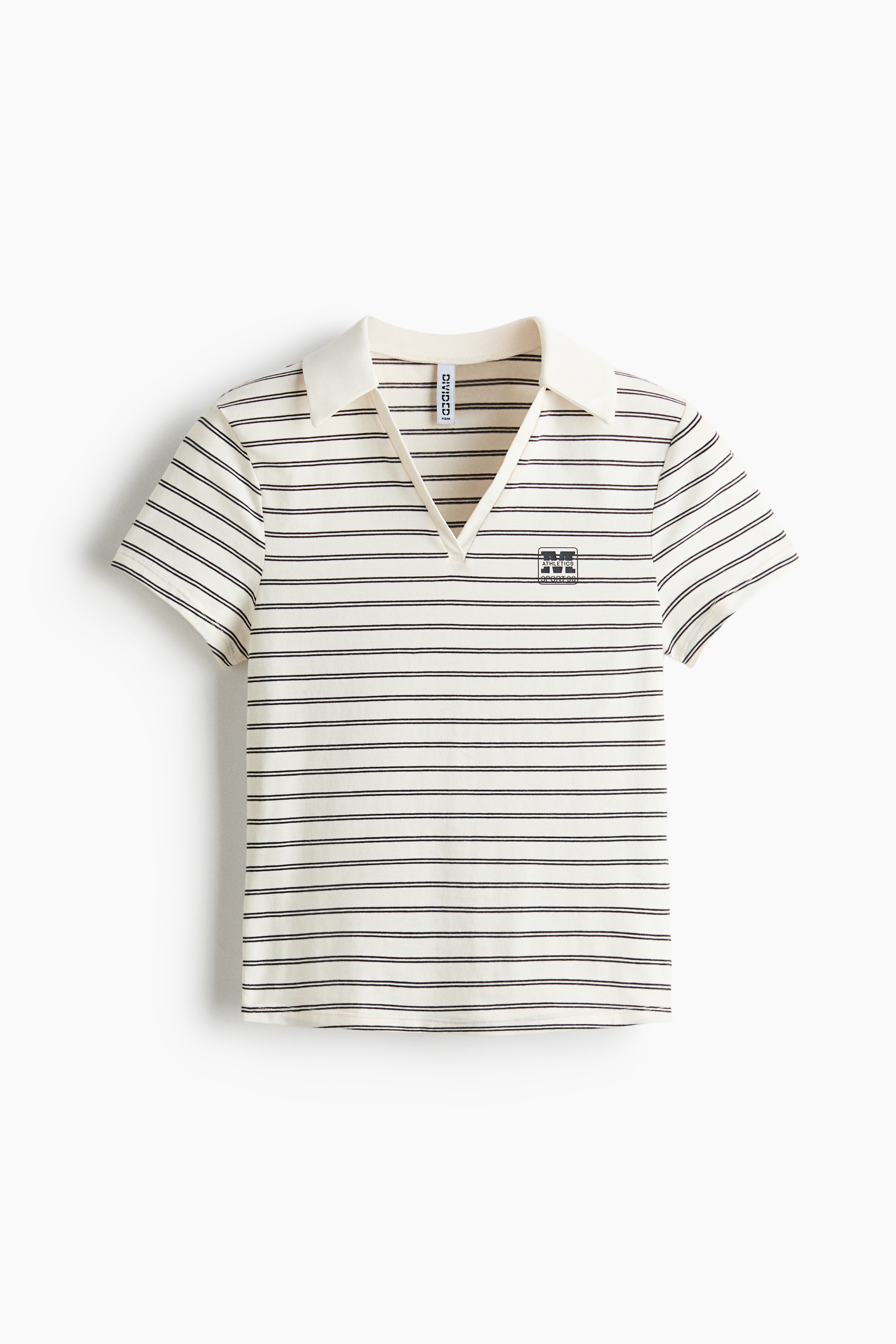 The polo shirt is shown from the front, highlighting a cream-colored cotton jersey fabric with thin horizontal black stripes and a small printed logo on the left chest. It features an open V-neck collar, short sleeves, and a straight-cut hem that sits just above the waistline of light-wash denim jeans.