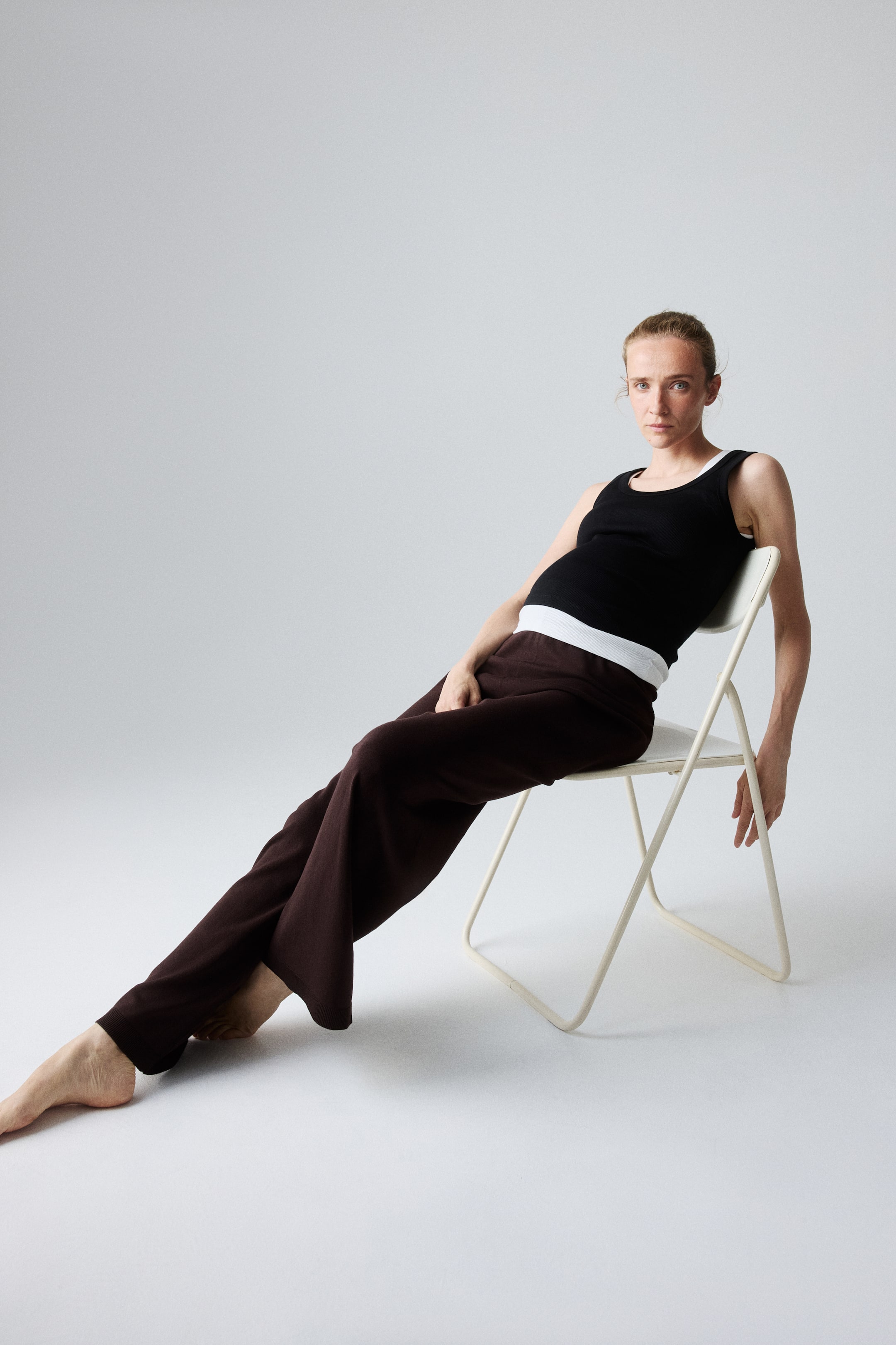 View larger image: Dark brown knitted trousers made from a viscose blend are worn by the model, featuring a high rib-trimmed waist and long, wide legs with ribbed hems. The model is seated with one leg extended.