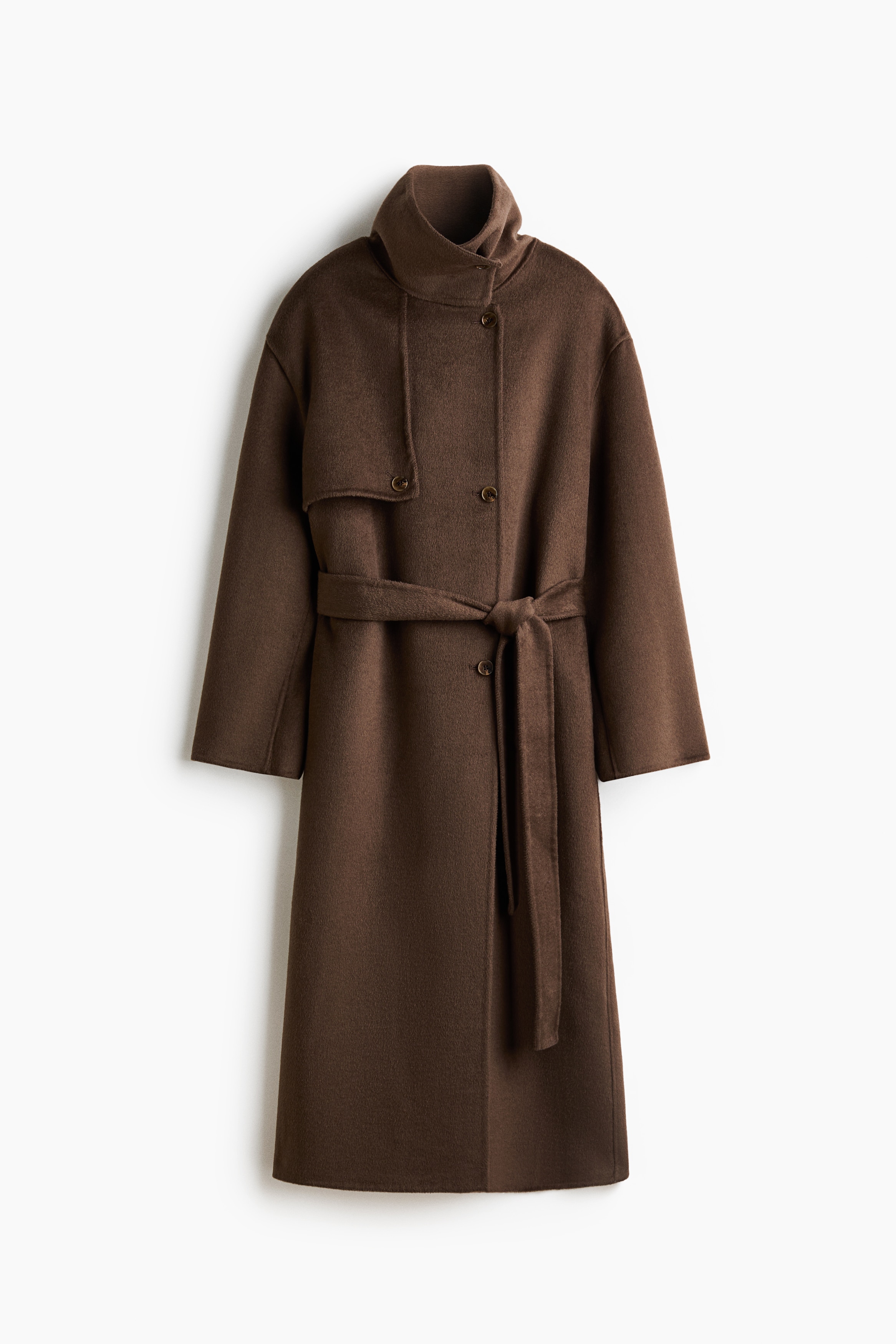 The model is wearing a dark brown, felted wool-blend coat featuring a high buttoned funnel collar, a buttoned storm flap across the chest and a matching tie belt at the waist. The model is holding a dark green, satin-like bag tucked under one arm.