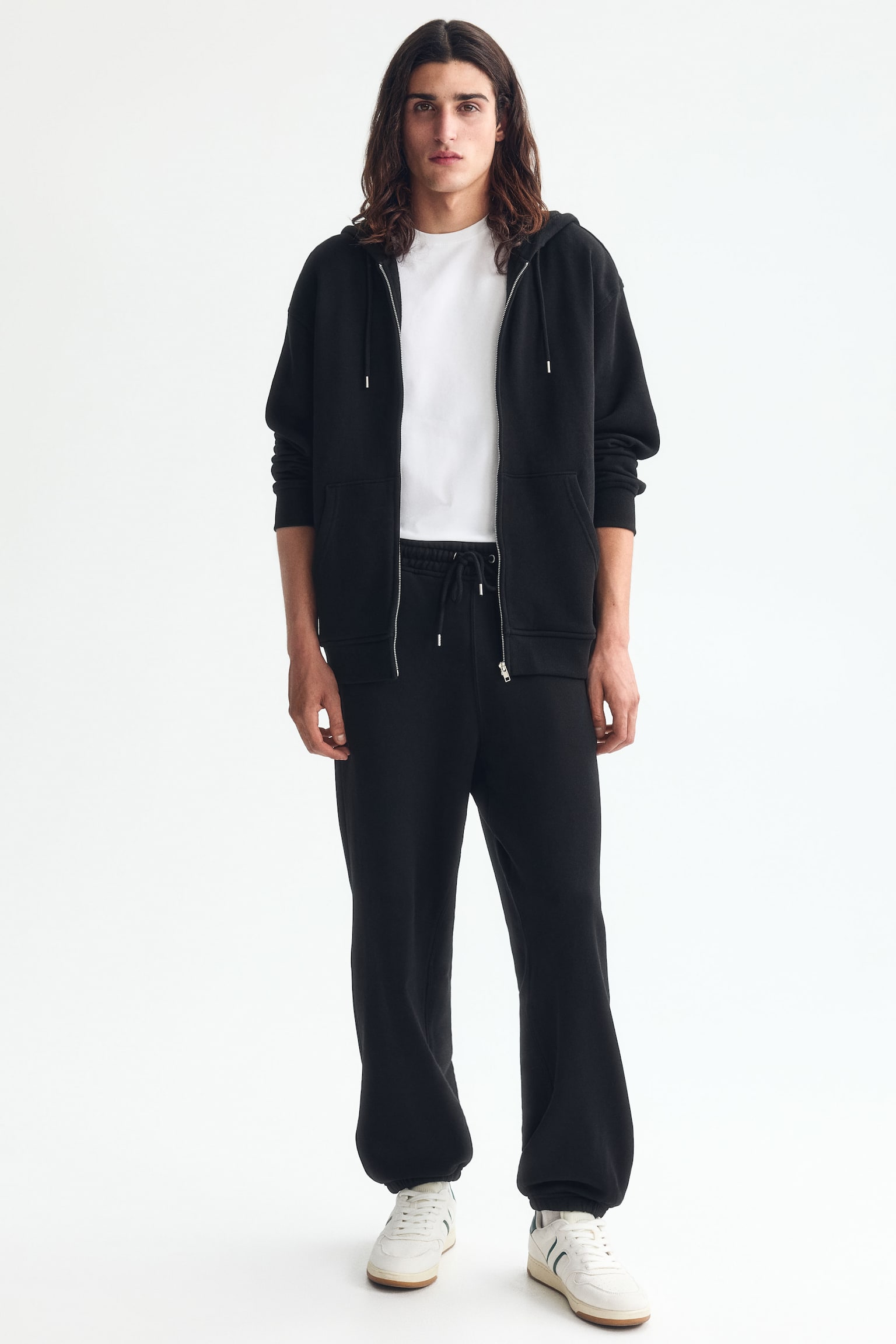 Black sweatpants in a cotton sweatshirt fabric are showcased from the front, featuring a covered elasticated waist with a drawstring and metal aglets. They offer a relaxed fit with discreet side seam pockets and elasticated hems. - 1
