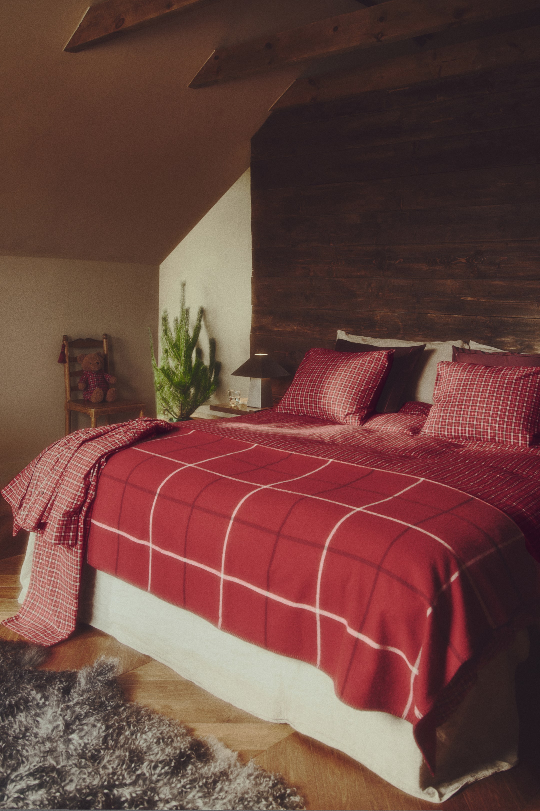 View larger image: A cotton flannel duvet cover set is dressing a bed from a front-facing angle, showcasing a small red-and-white check pattern on the duvet cover and two matching pillowcases. The bedding is layered with a red blanket featuring a large white grid pattern draped over the lower half.