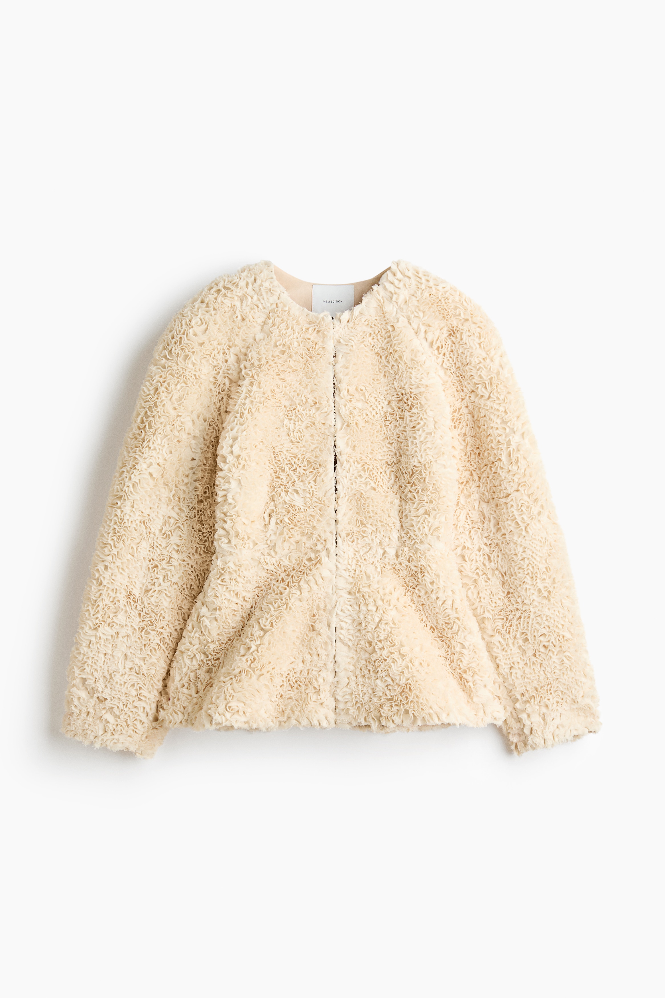 Une veste couleur crÃ¨me, dotÃ©e dâune texture dense et volantÃ©e ainsi que dâun bas peplum Ã©vasÃ©, est portÃ©e par le mannequin, qui a les mains posÃ©es sur les hanches. La veste est associÃ©e Ã  une jupe assortie Ã  volants superposÃ©s.