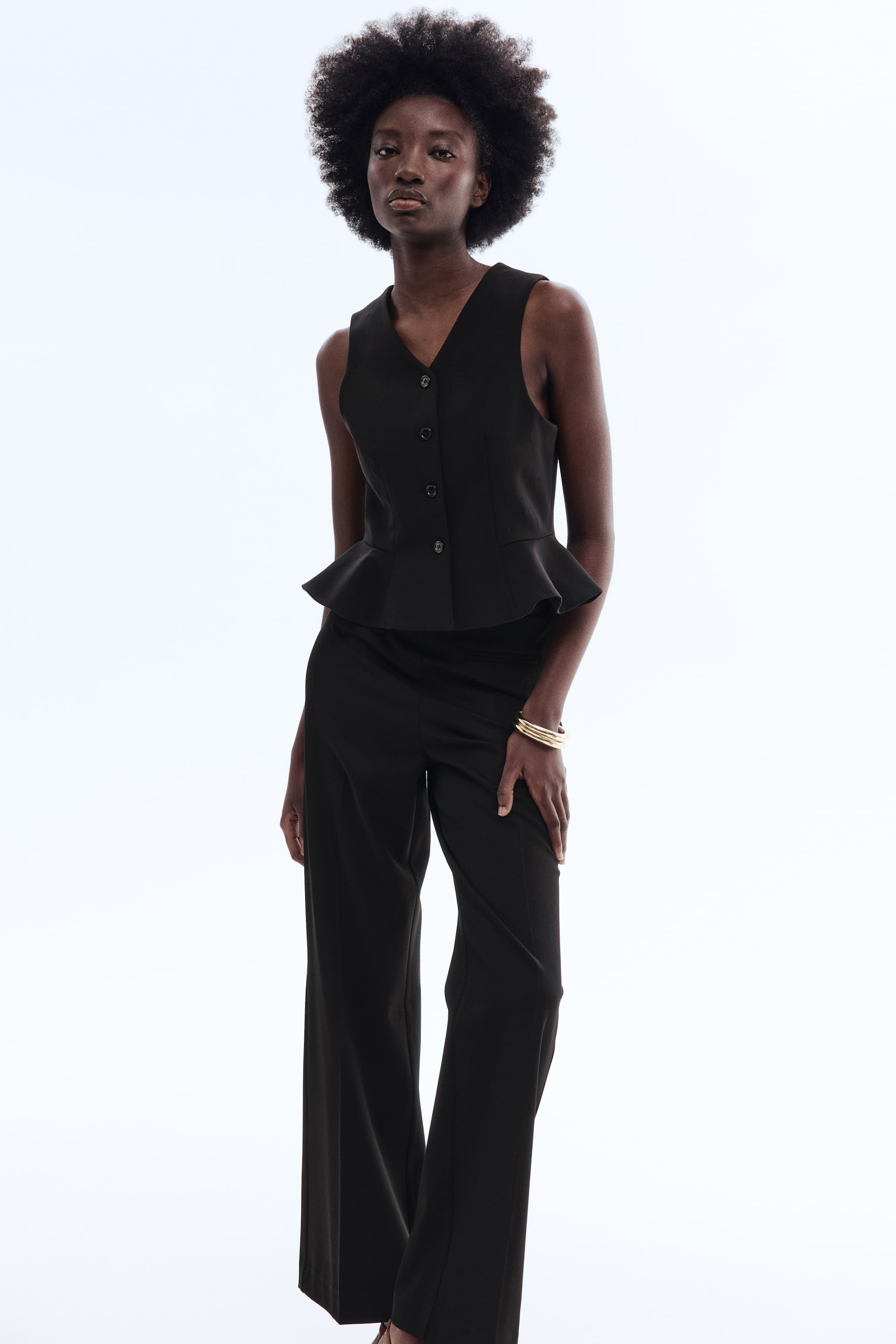 View larger image: A black sleeveless peplum top featuring a V-neckline and button-front closure, with its peplum hem flaring at the waist. It is paired with matching black wide-leg trousers.