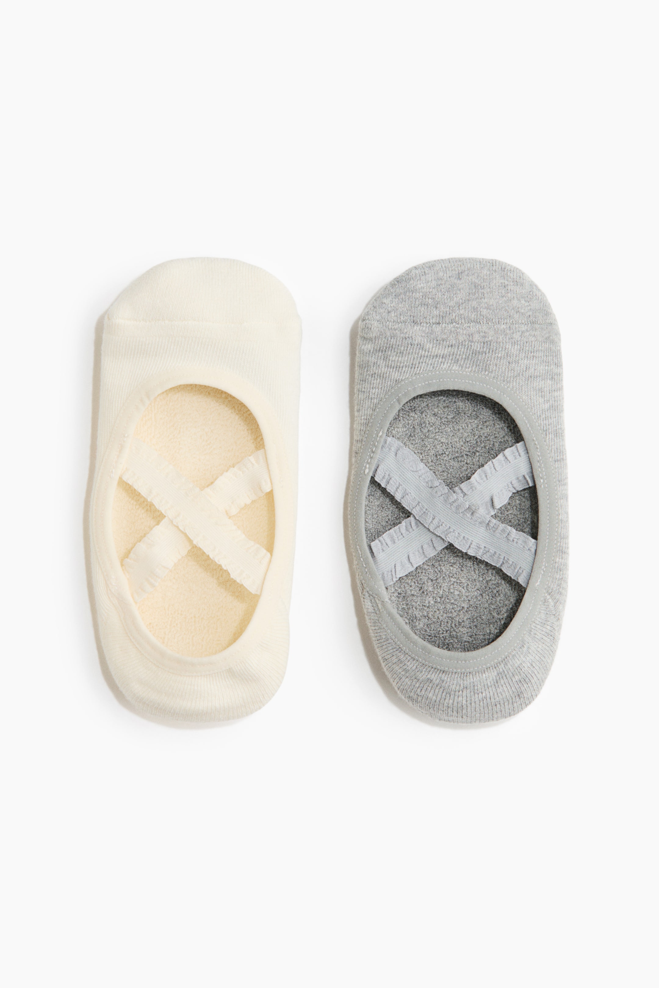 View larger image: Two low-cut studio socks, one in off-white and one in light grey, are lying side by side facing front to show their design. Each sock features a deep opening with elasticated binding, ruffled criss-cross elastic straps over the foot, and a visible soft terry lining inside.