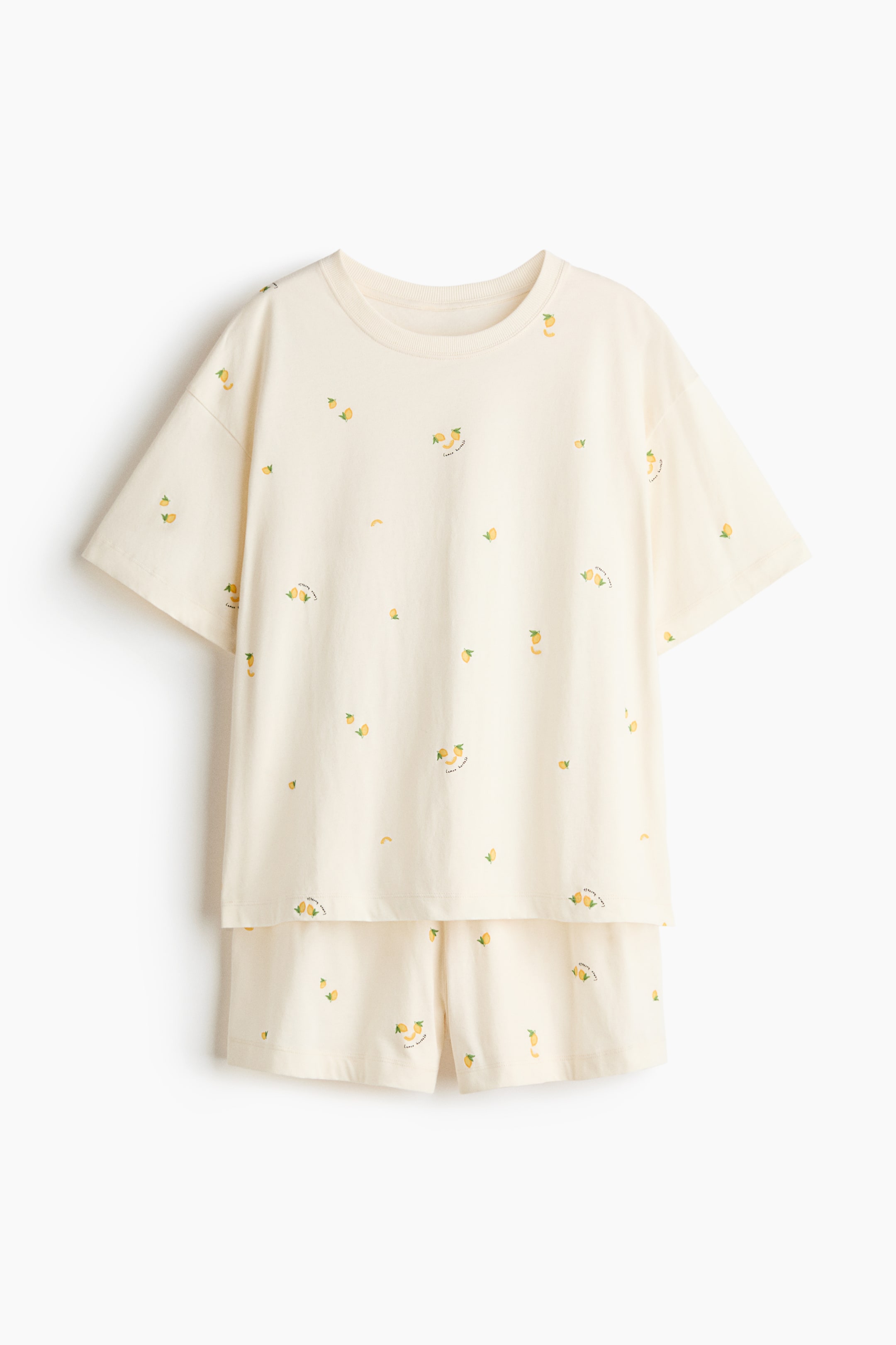 View larger image: A pajama set, front-facing, showcases a T-shirt and shorts in soft cotton jersey, both adorned with a printed pattern of small yellow lemons and "lemonade" text. The T-shirt features a ribbed trim around its neckline and dropped shoulders, while the shorts have covered elastic at the waist.