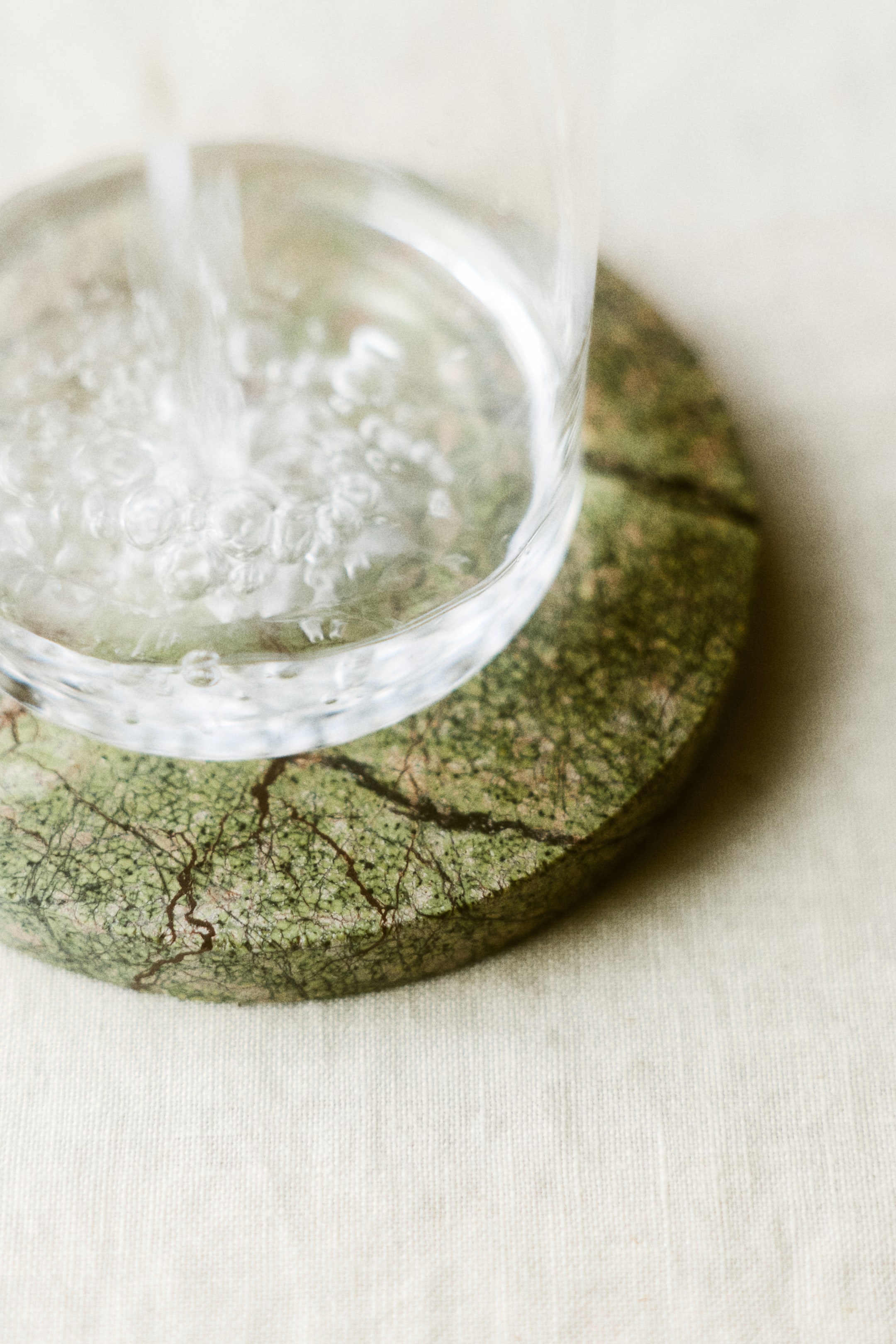 View larger image: A round green marble coaster with dark veining is holding a clear glass. Water is being poured into the glass, creating bubbles.