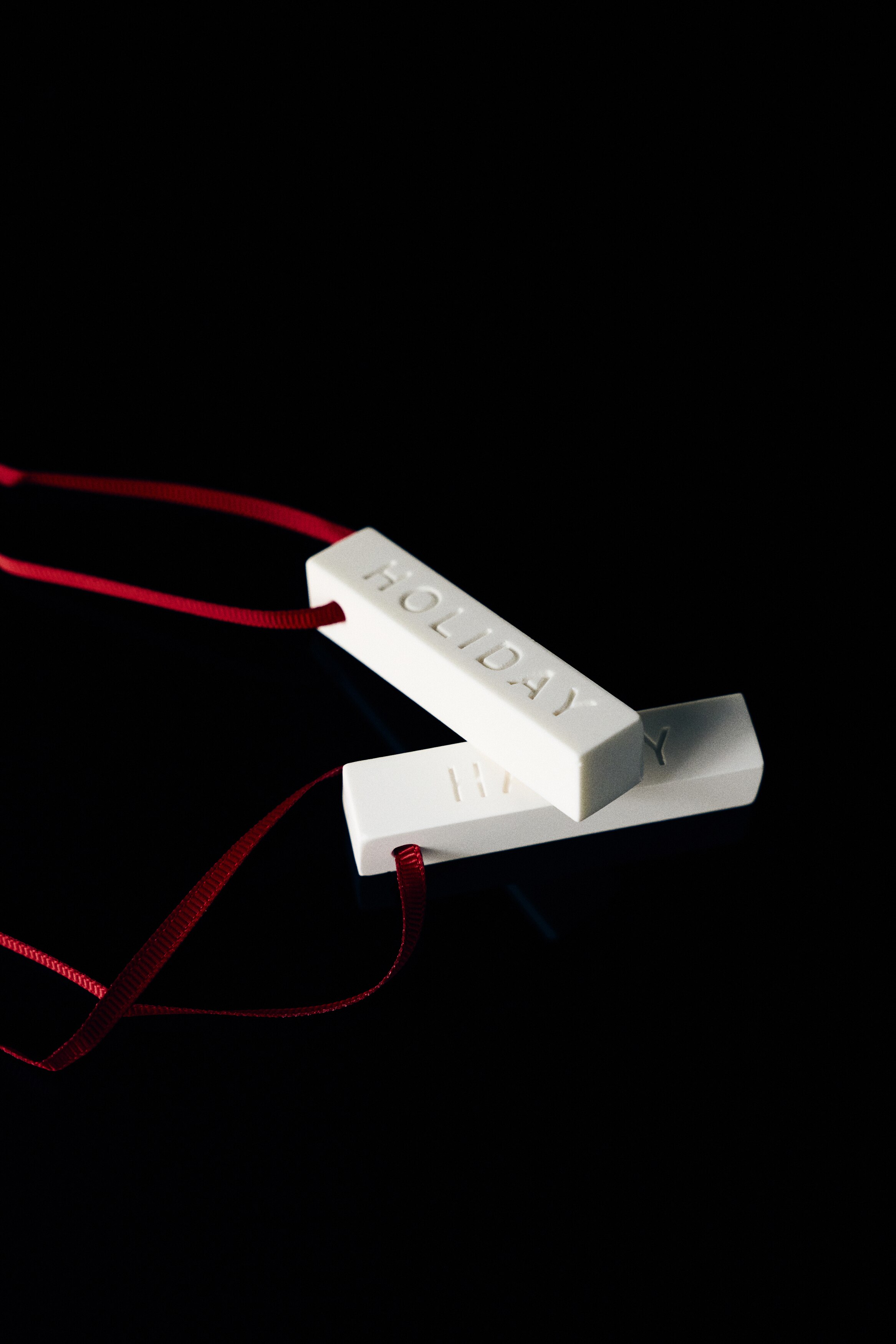 A scented bar gift set is presented in an open textured red box with its matching lid facing front in a flat lay perspective. The lid features a scattered pattern of small gold-foiled reindeer and a central label, while the open compartment holds three white rectangular wax bars embossed with the words "HAPPY", "HAPPY", and "HOLIDAY".