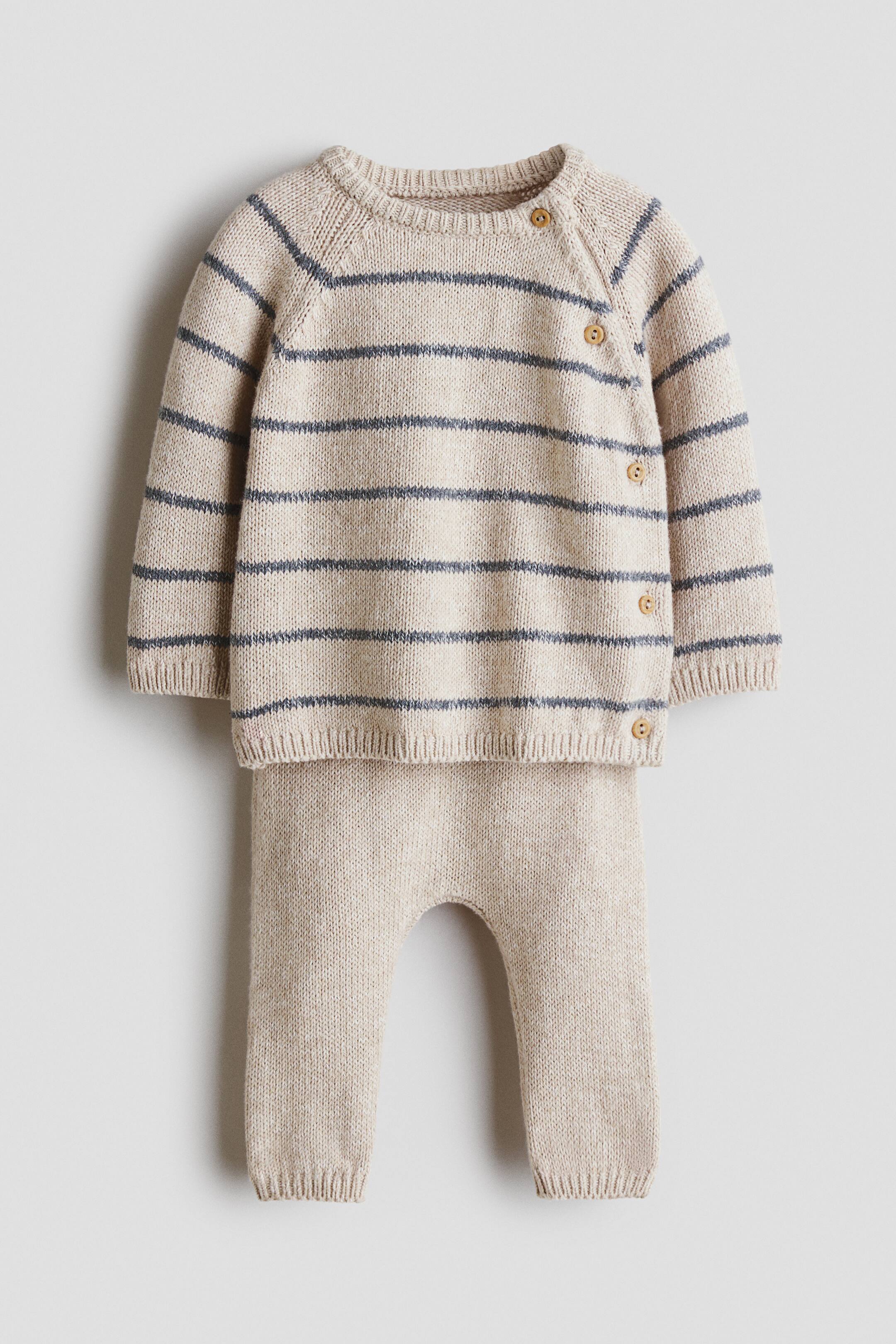 View larger image: A fine-knit set, shown from the front, featuring a light beige jumper with horizontal dark blue stripes, a round ribbed neckline, long raglan sleeves, and a side opening with four buttons. The jumper is finished with ribbed cuffs and hem, and is complemented by matching light beige trousers with ribbed hems.