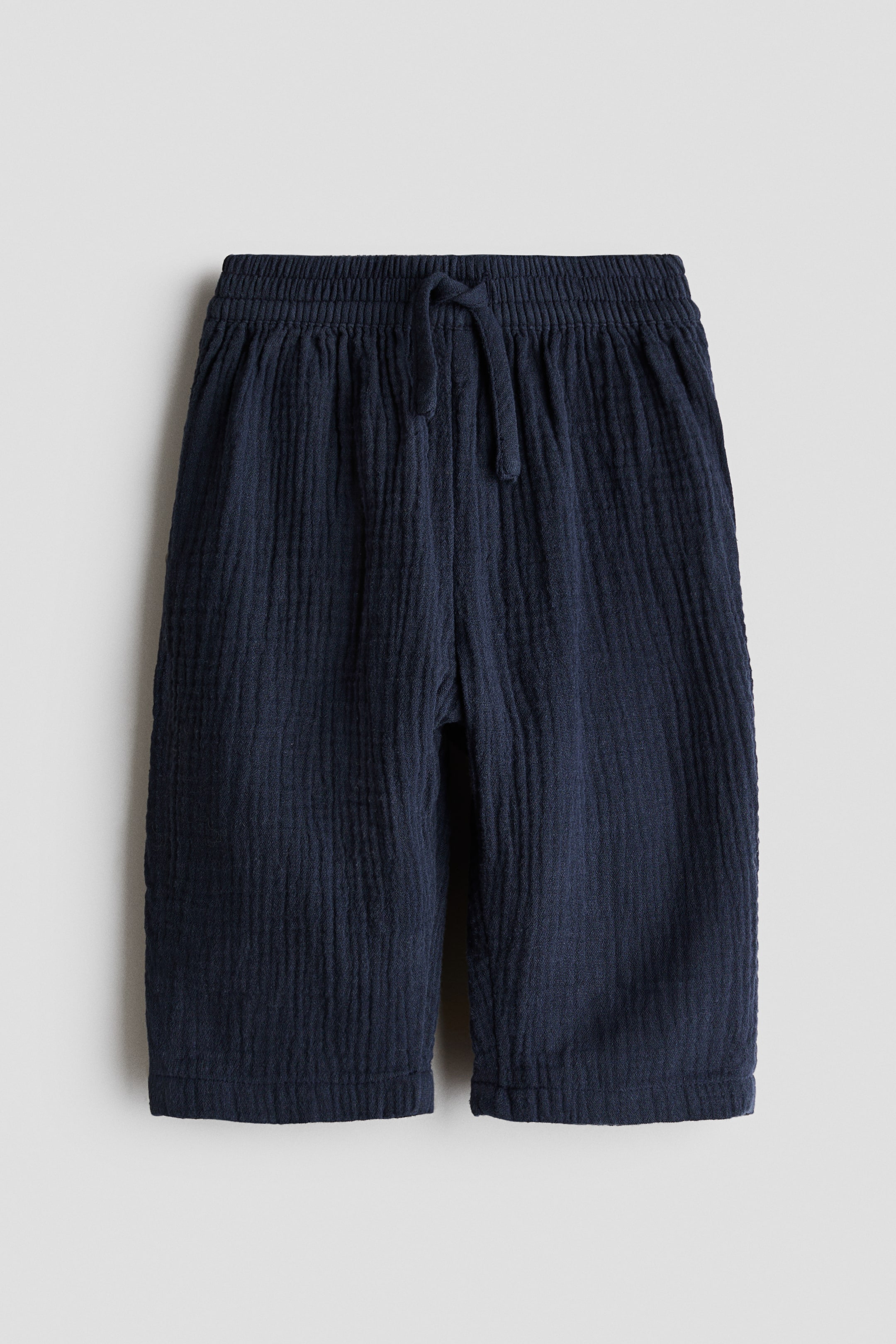 Ampliar la imagen: Los pantalones Adorables de H&M se presentan desde el frente, mostrando una textura arrugada de color azul oscuro. Presentan un ajuste holgado con una pretina elástica y un cordón ajustable atado al frente.