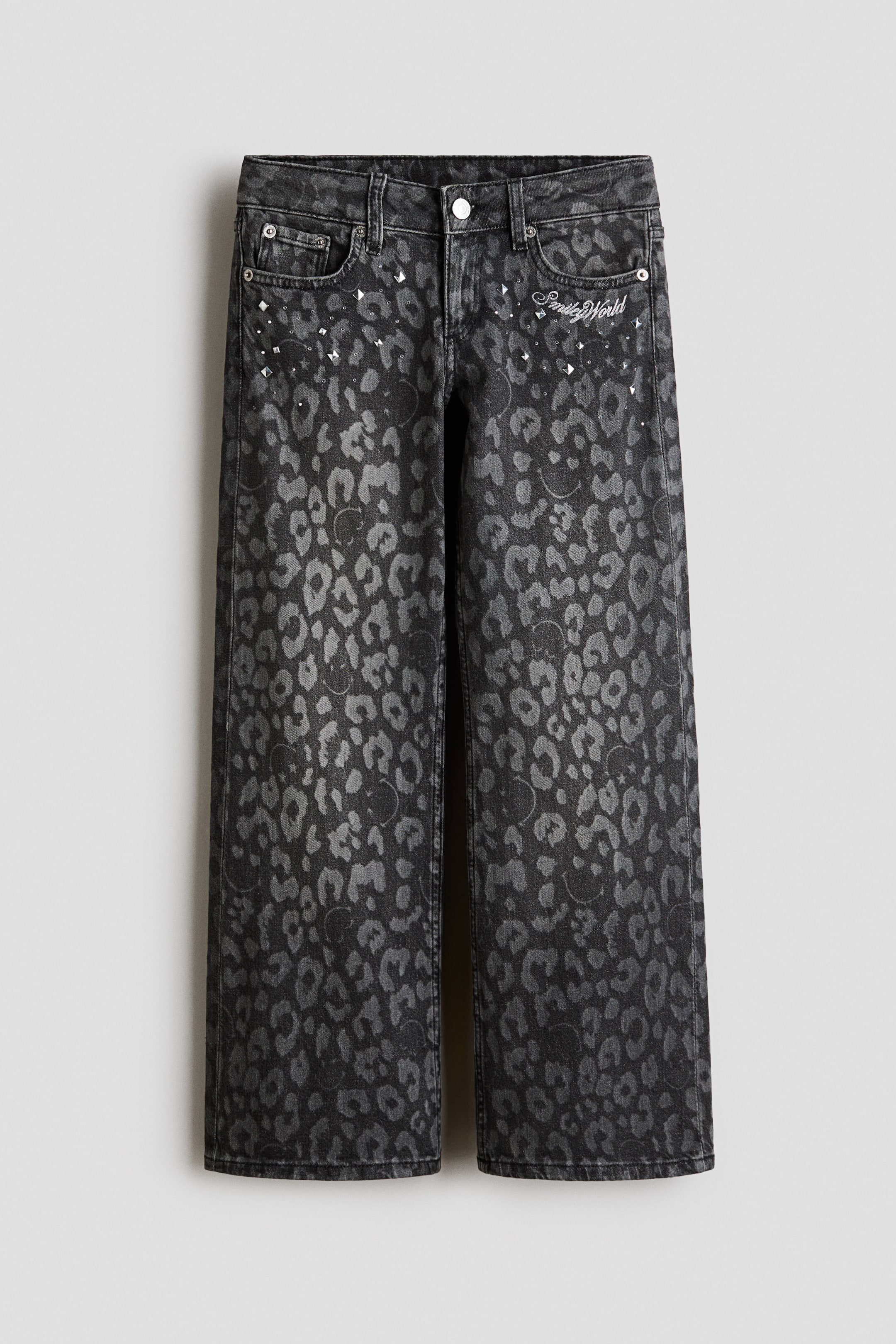 Voir une image plus grande: Les jeans présentent un délavage gris foncé avec un imprimé léopard gris clair intégrant subtilement des motifs de visages souriants. Cette paire à jambes larges dispose d'une ceinture standard, de passants pour ceinture, d'une fermeture à bouton, d'une braguette zippée, et de poches avant ornées de rivets argentés et de clous transparents épars, tandis que "Smiley World" est brodé en blanc au-dessus de la poche avant droite.
