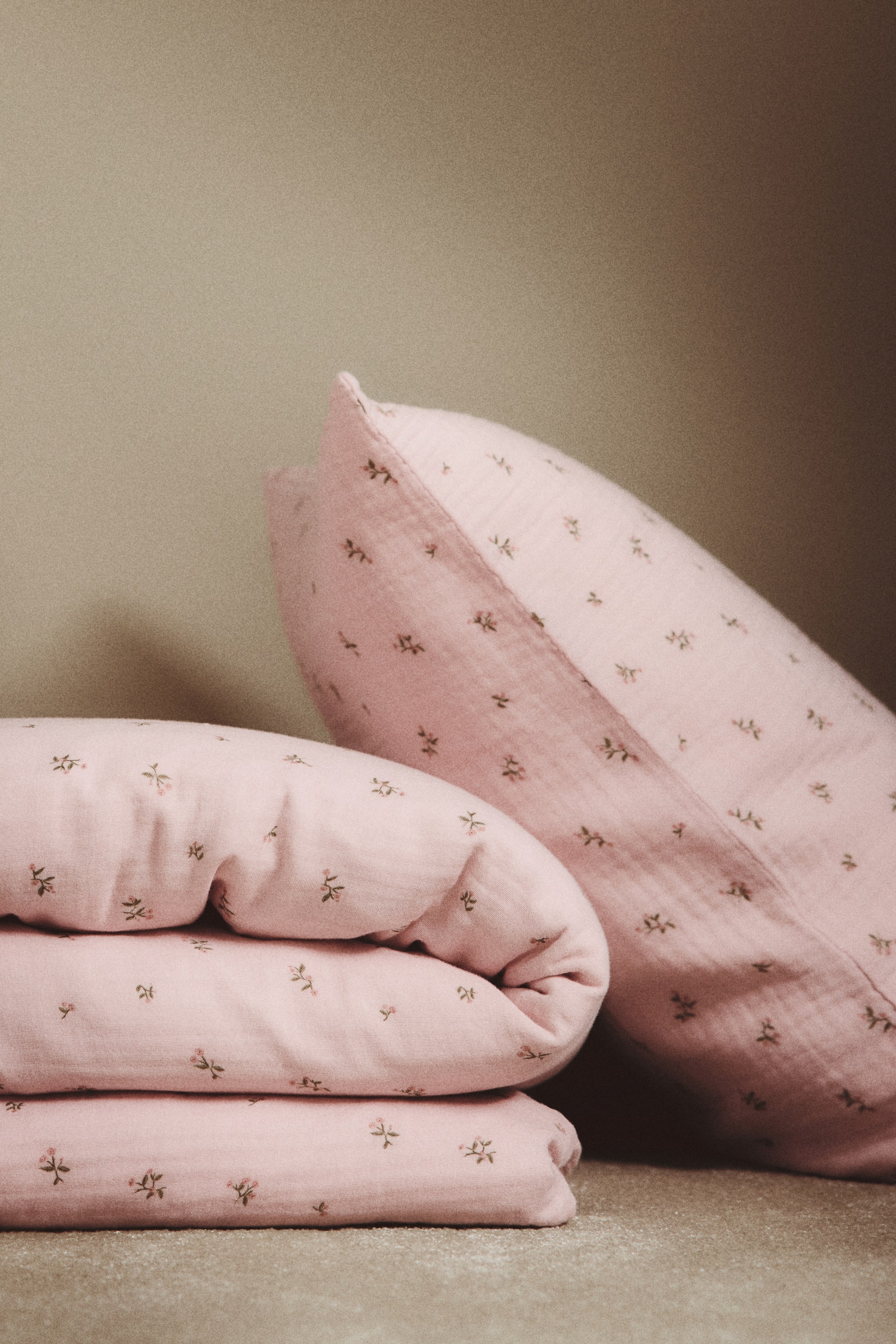 View larger image: A pink cotton muslin duvet cover set features a small all-over floral print. The duvet cover is folded to display its front, with a matching pillowcase positioned at an angle behind it.
