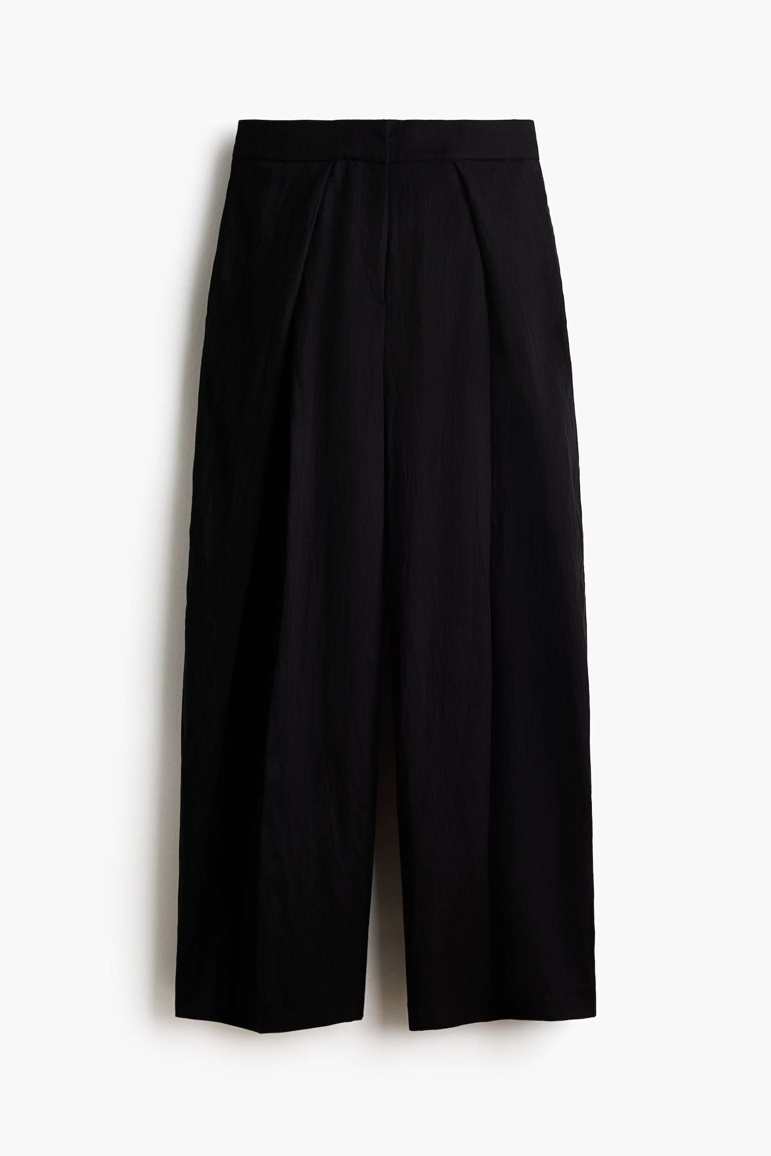 Pantalones negros con una cintura plana y pliegues debajo, que se extienden hacia unas piernas anchas y recortadas. La tela presenta una sutil textura arrugada. - 1