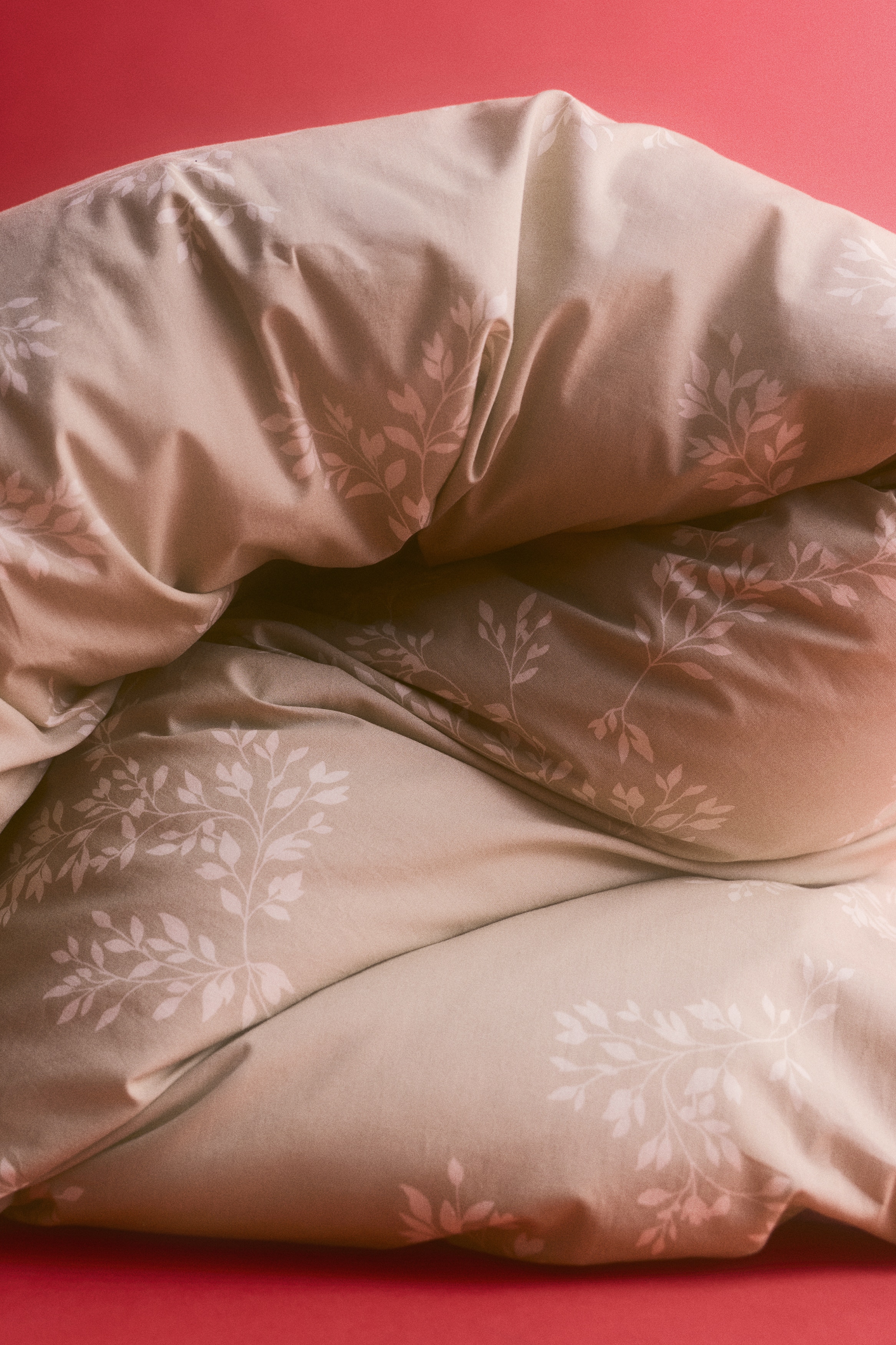 Un ensemble de literie beige prÃ©sente un motif botanique de feuilles blanches, vu de face. Lâensemble comprend deux taies dâoreiller assorties, dressÃ©es Ã  la verticale derriÃ¨re une housse de couette soigneusement pliÃ©e.