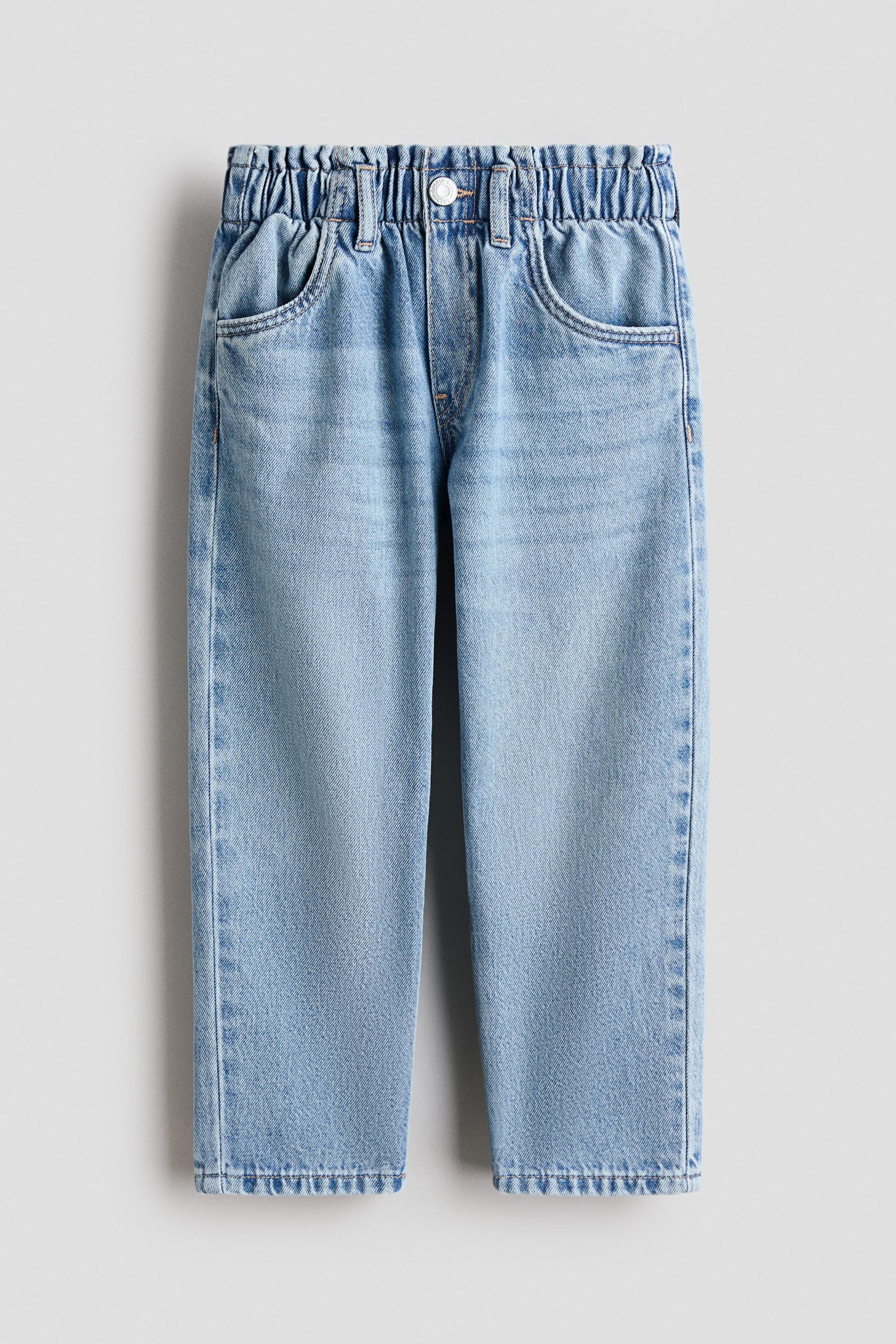 View larger image: Light-blue cotton denim jeans are shown from the front, featuring a loose fit through the hips and thighs. They are designed with an elasticated paper-bag waist, a fake fly with a press-stud, diagonal side pockets, and gently tapered legs.