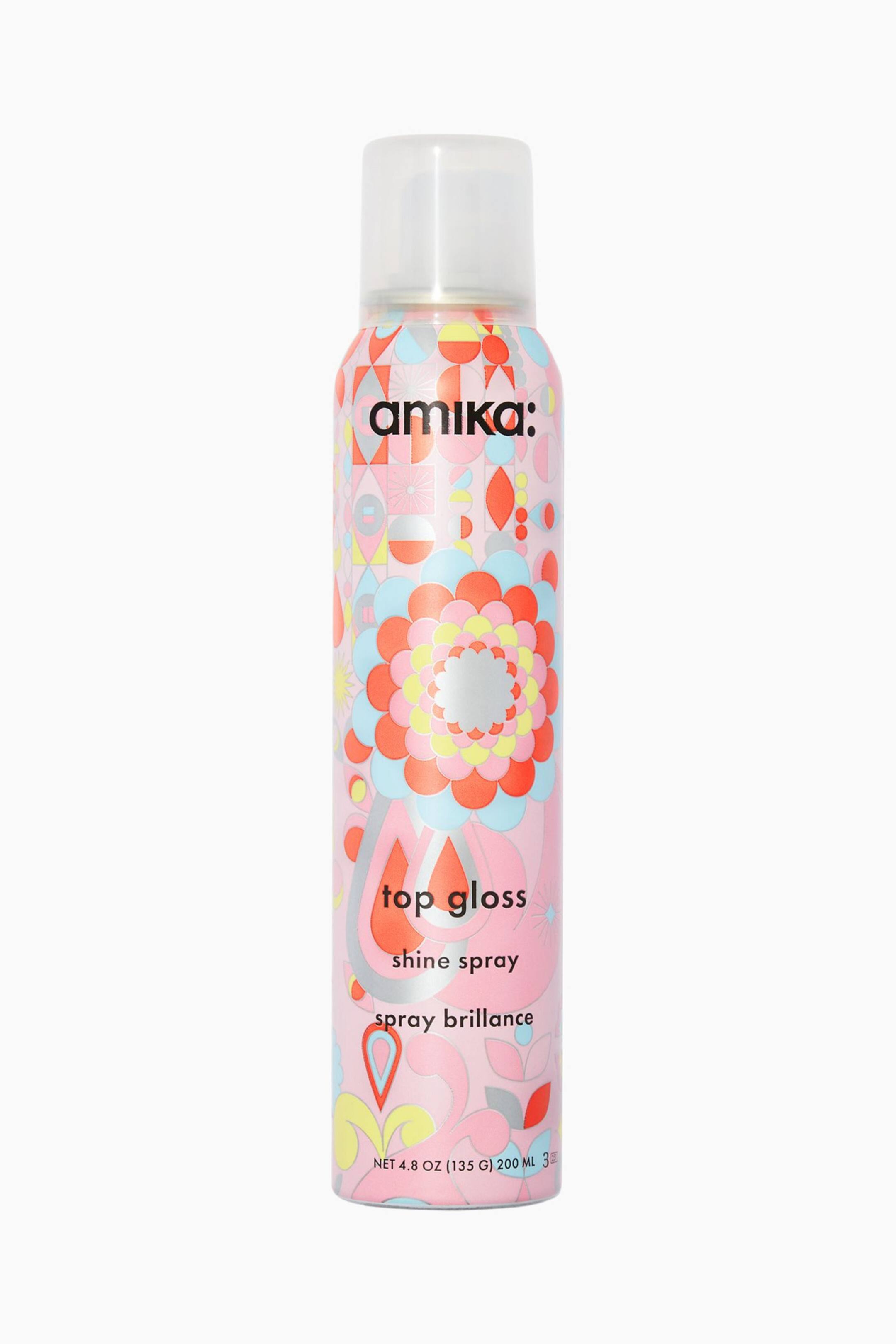 Visa större bild: En upprätt aerosolburk med amika: Top Gloss Shine Spray står vertikalt och har en genomskinlig kork och en ljusrosa kropp dekorerad med ett livfullt, retroinspirerat mönster av geometriska och blommiga former. På burkens framsida visas varumärket "amika:" och produktnamnet "top gloss shine spray" i svart text med gemener.