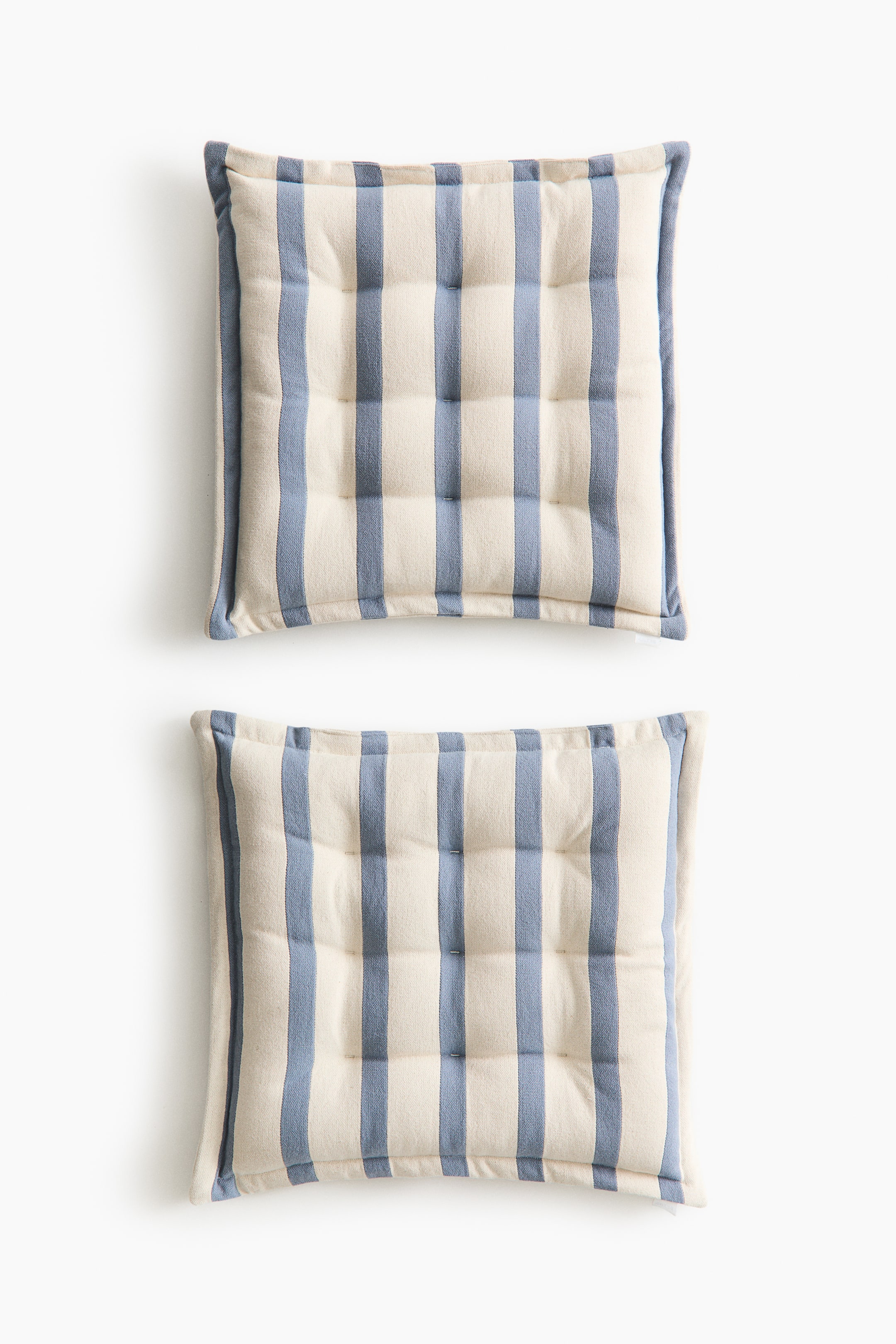 View larger image: A pair of padded seat cushions in cotton canvas showcase a pattern of vertical cream and light blue stripes. They also feature quilt knots and a border around their edges.