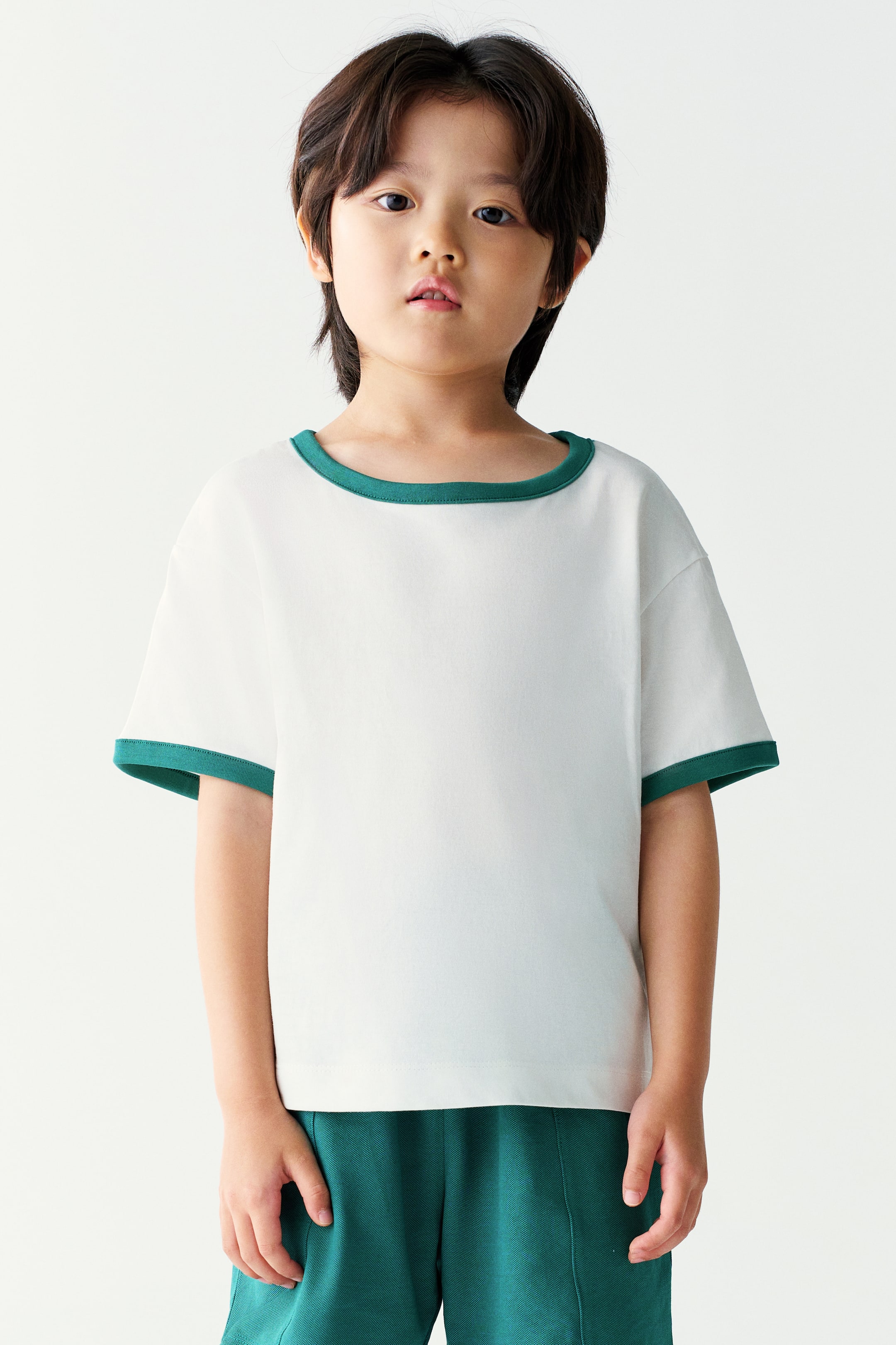 View larger image: A white ringer T-shirt with green trim along the neckline and sleeve cuffs is worn by the model. The short-sleeved top is paired with matching green shorts.