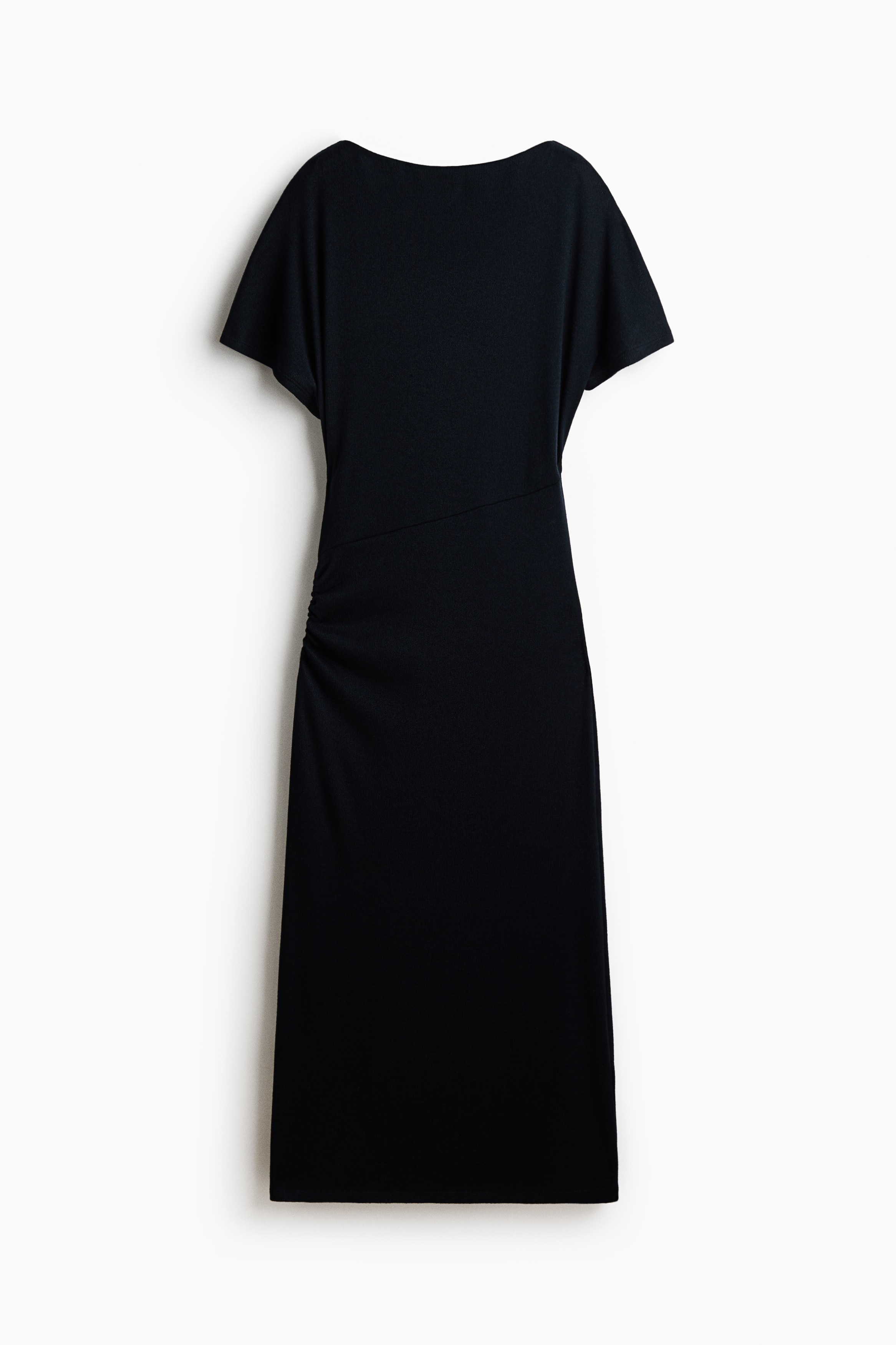 The model is wearing a long black knit dress featuring a delicate boat neck, a relaxed-fit bodice, and short butterfly sleeves. The dress has a diagonal waist seam with gathering at the hip, flowing down to an ankle-length hem.