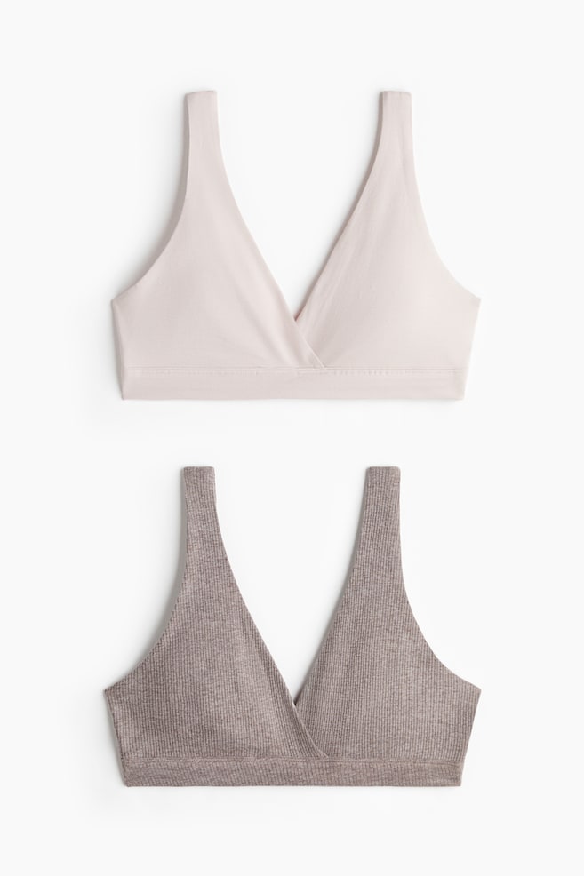 Two soft, non-wired nursing bras are presenting their FRONT, stacked vertically, with the top bra featuring smooth, light beige fabric and the bottom bra showcasing a ribbed, muted brown texture. Both bras are designed with wide shoulder straps and a wrapover front, with no visible fasteners. - 1