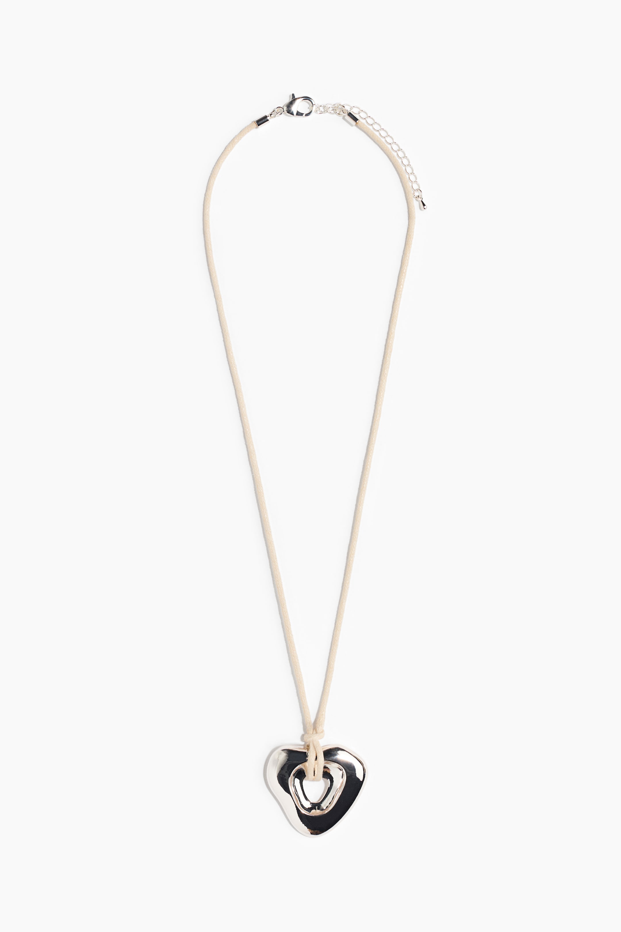 View larger image: A necklace is presenting a light beige cord, FRONT facing, suspending a silver-toned, irregularly shaped heart pendant with an open center. A silver-toned lobster clasp and extender chain are securing the cord.