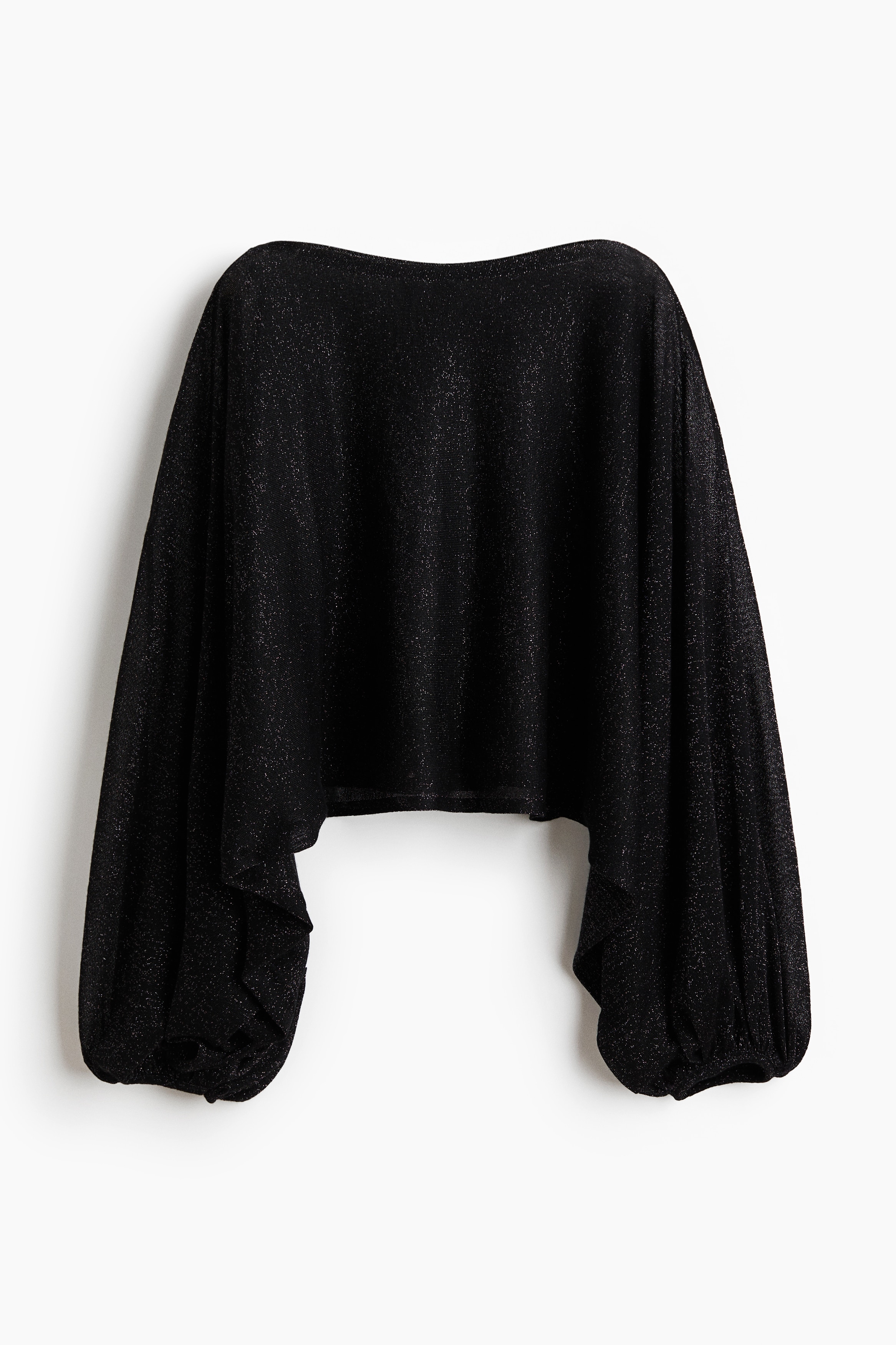 Ein kurzes, oversized schwarzes Stricktop mit glitzernden Fäden wird vom Model getragen und verfügt über einen U-Boot-Ausschnitt sowie lange, voluminöse Cape-Ärmel mit schmalen, elastischen Bündchen. Das leicht transparente Top ist mit einer passenden weiten Hose kombiniert, während das Model eine Hand in die Taille legt.