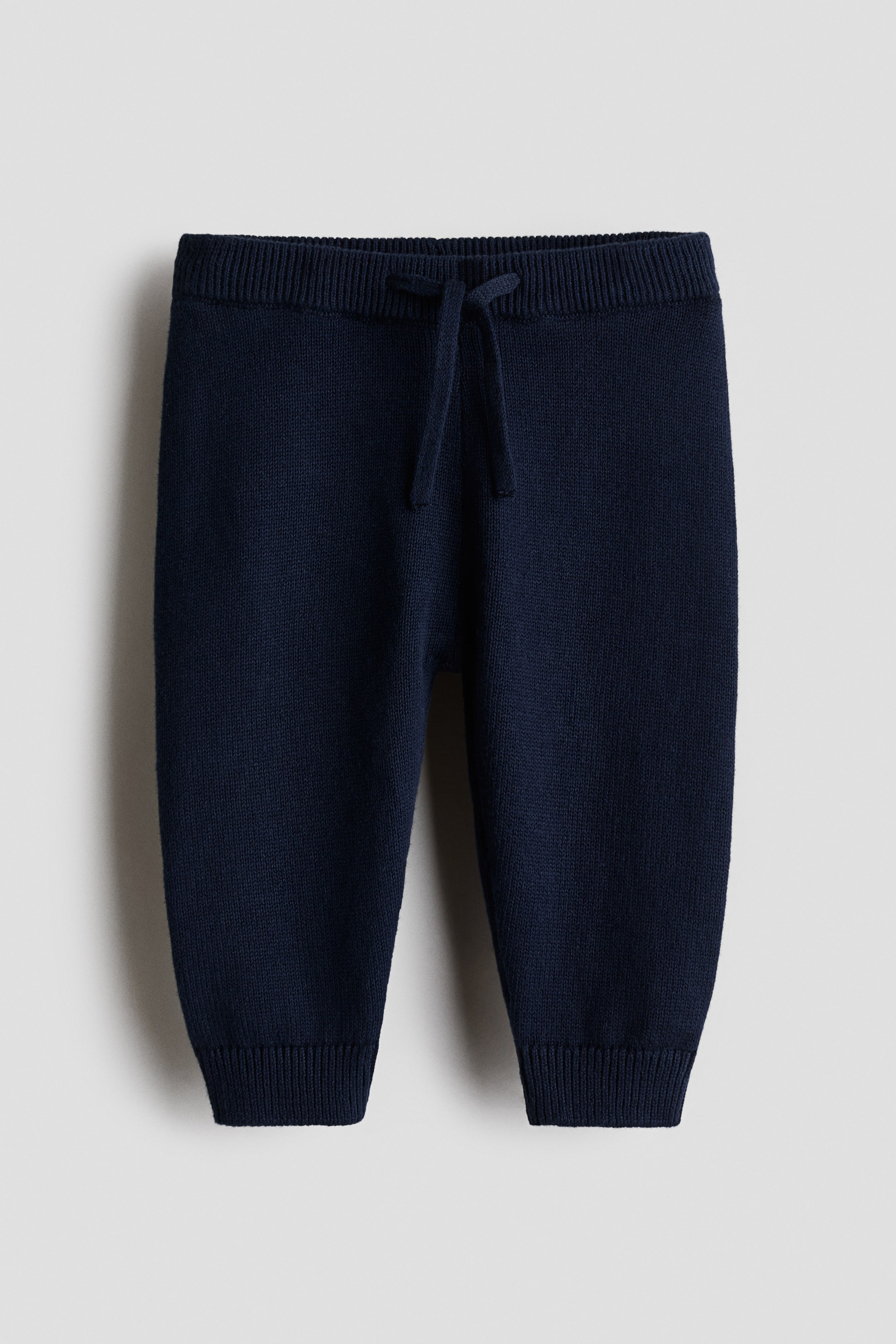 Grotere afbeelding bekijken: Marineblauwe gebreide broek, van voren weergegeven, met een geribde tailleband met trekkoord en geribde enkelboorden.
