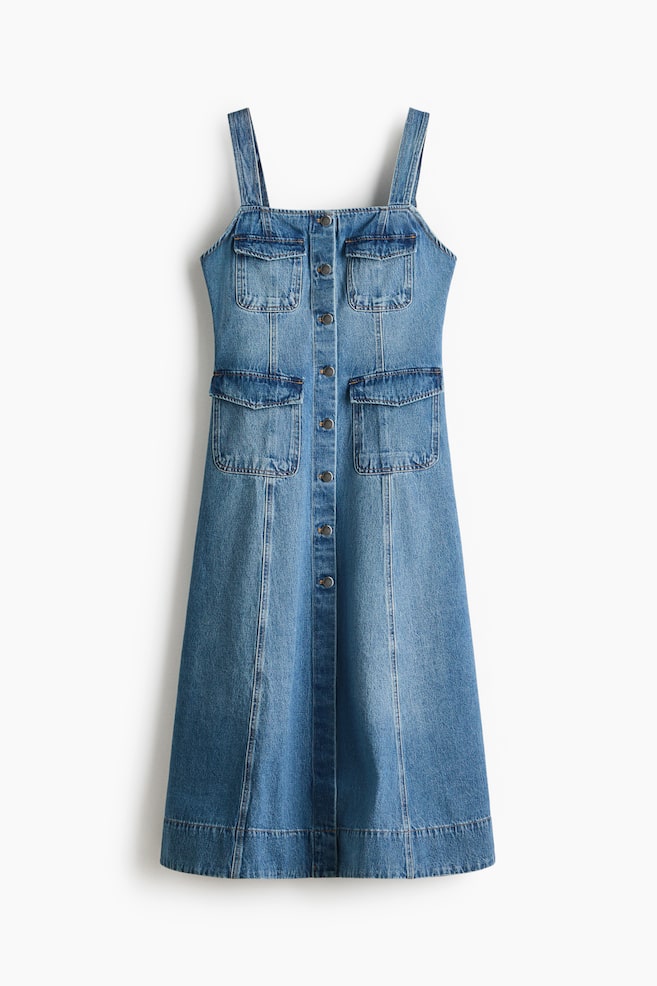 A front-facing medium blue denim dress featuring wide shoulder straps, a full button-down front with dark buttons, and four flap pockets, with two on the chest and two lower on the hips. Vertical seam detailing runs down the midi-length skirt, finishing with a wide hem. - 1