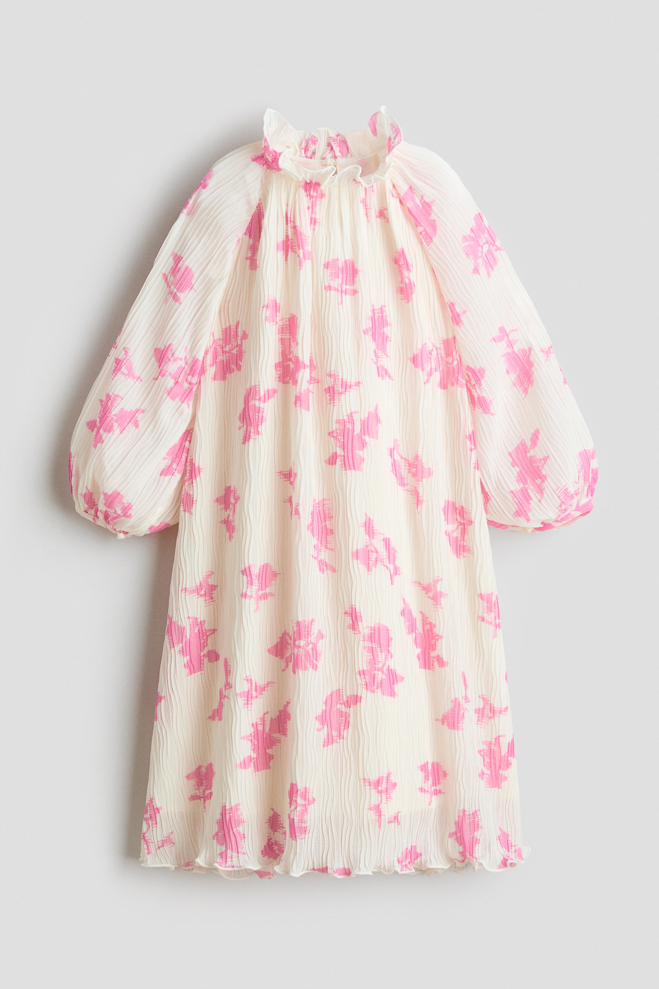 Büyük resmi görüntüle: Bu elbisenin önü, soyut pembe desenlerle kaplı kırık beyaz, buruşuk bir kumaş sunuyor. Yüksek fırfırlı bir yaka, manşetlerde toplanmış uzun hacimli kollar ve fırfırlı bir etek ucu ile tasarlanmıştır.