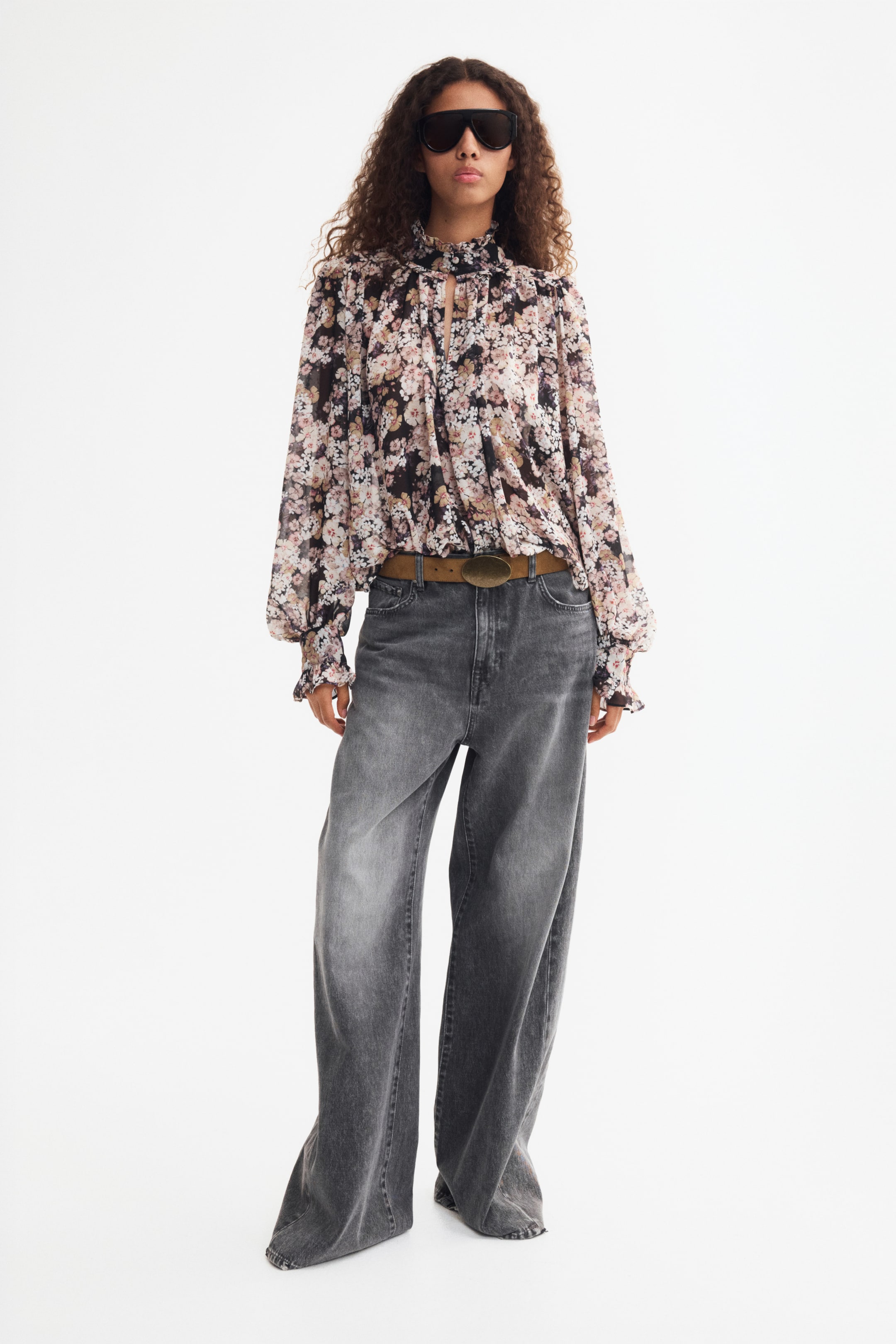 Größeres Bild ansehen: Eine Chiffonbluse mit Puffärmeln und dunklem Blumenprint wird vom Model getragen und in eine weit geschnittene graue Jeans gesteckt. Die Bluse verfügt über einen hohen, gerafften Kragen mit Schlüsselloch-Detail sowie lange, voluminöse Ärmel mit elastischen, gerafften Bündchen.