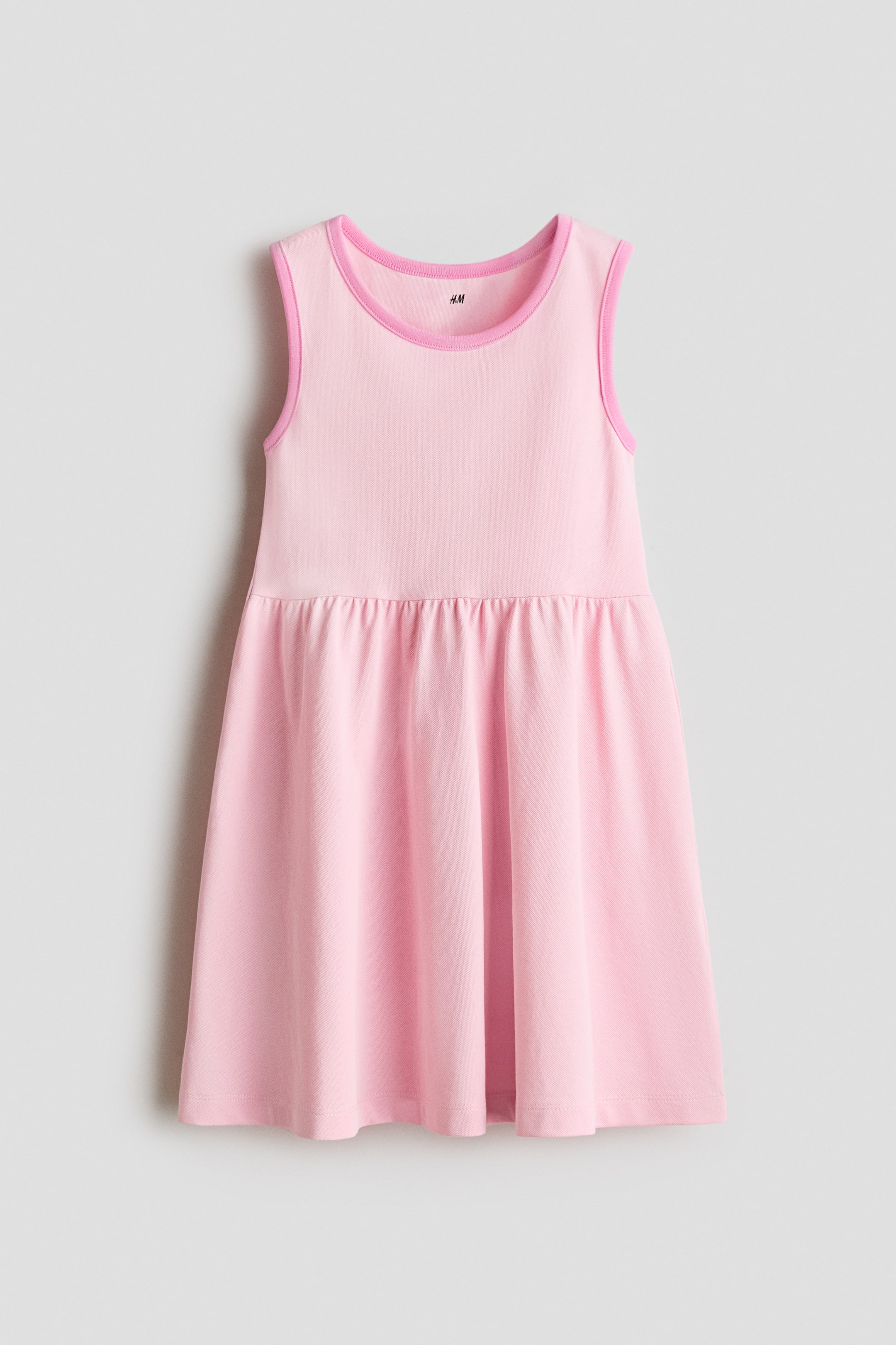 View larger image: A light pink sleeveless dress featuring a round neckline and armholes with brighter pink piping tracing their edges. It presents a gathered waist seam leading to a flared skirt. The H&M label is visible inside the neckline.