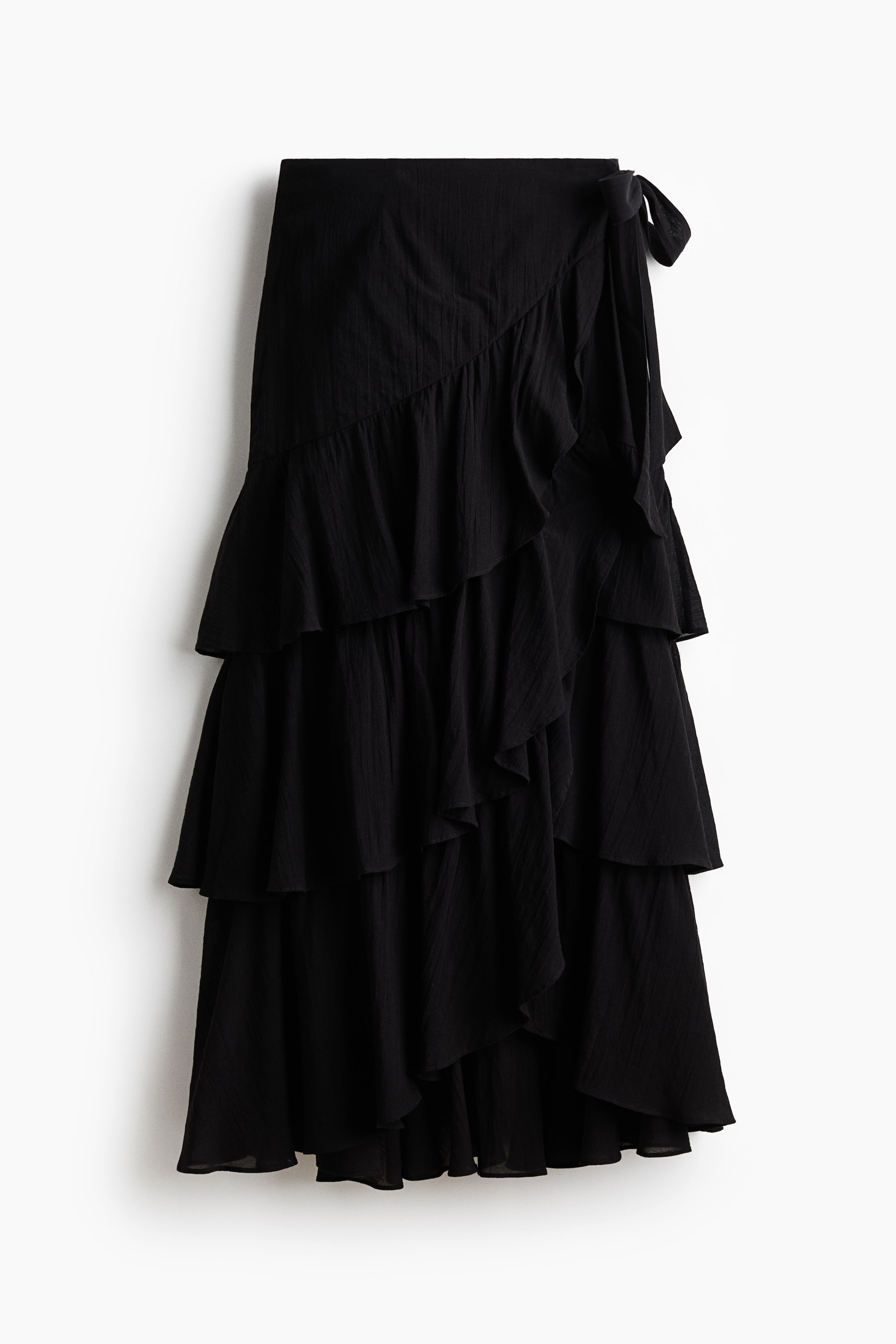 View larger image: A black ankle-length skirt featuring a wrapover front, with wide ties knotted on the right side. The skirt showcases multiple asymmetric, flounced tiers that add volume to its overall design.