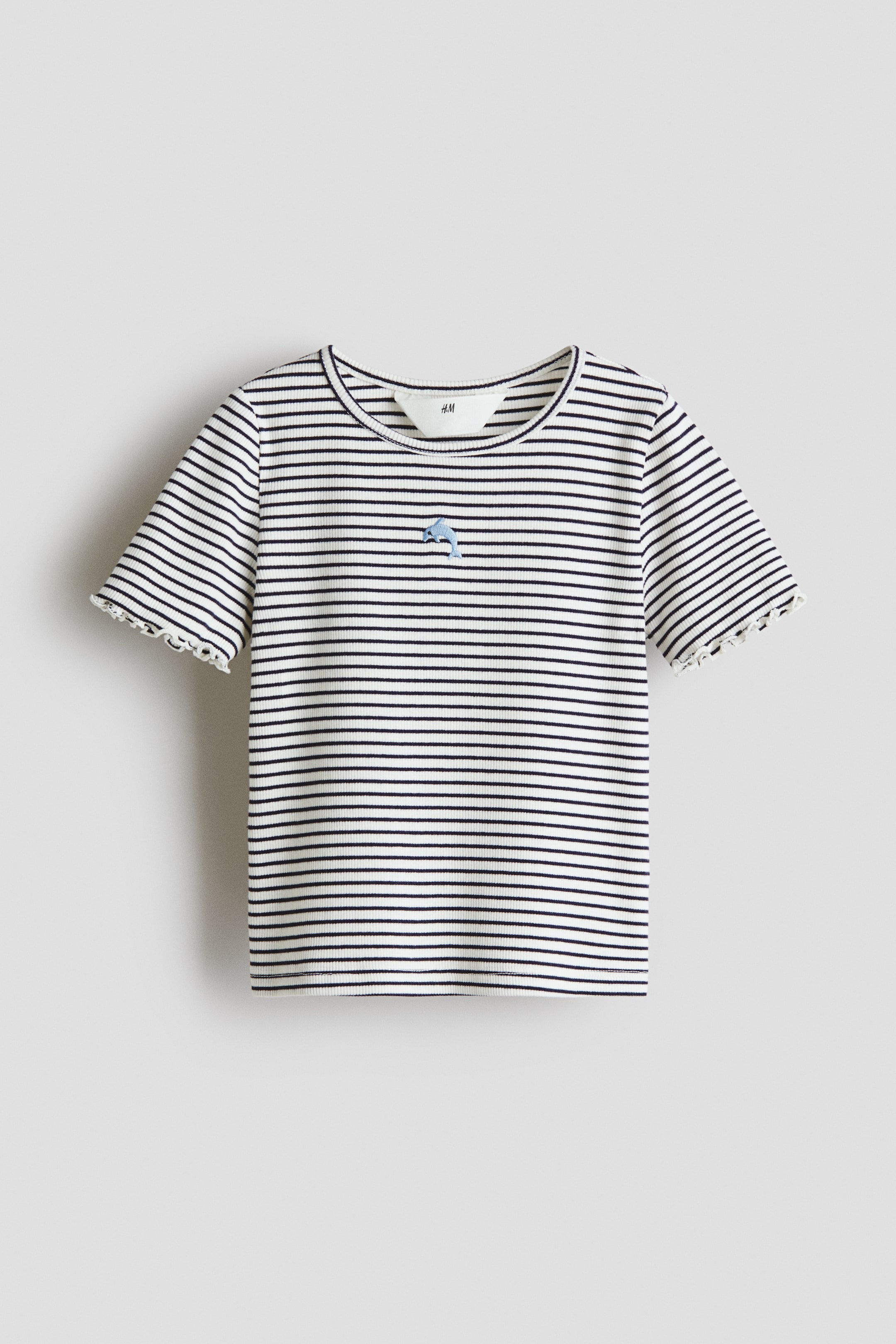 View larger image: A T-shirt is shown from the front, featuring a white ribbed fabric adorned with thin horizontal dark stripes. It is crafted with a round neckline, short sleeves with scalloped hems, and a small blue dolphin embroidery positioned on the left chest.