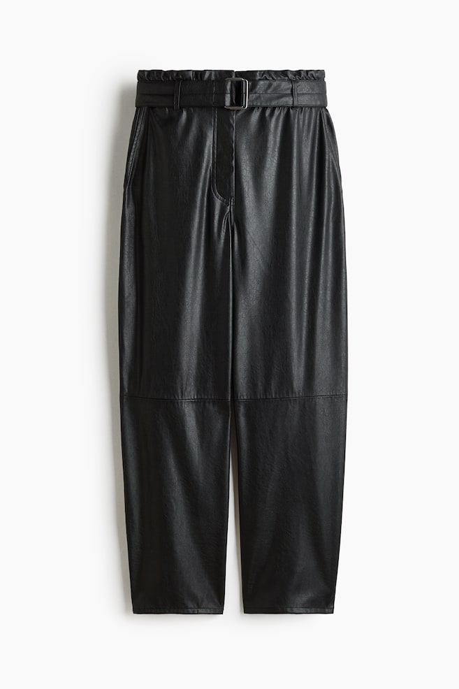 Un pantalon noir en faux cuir est présenté de face, avec une taille paperbag haute, une ceinture assortie ajustable et une boucle rectangulaire argentée. Le pantalon présente une coupe droite et décontractée, avec des détails de coutures horizontales au niveau des genoux. - 1
