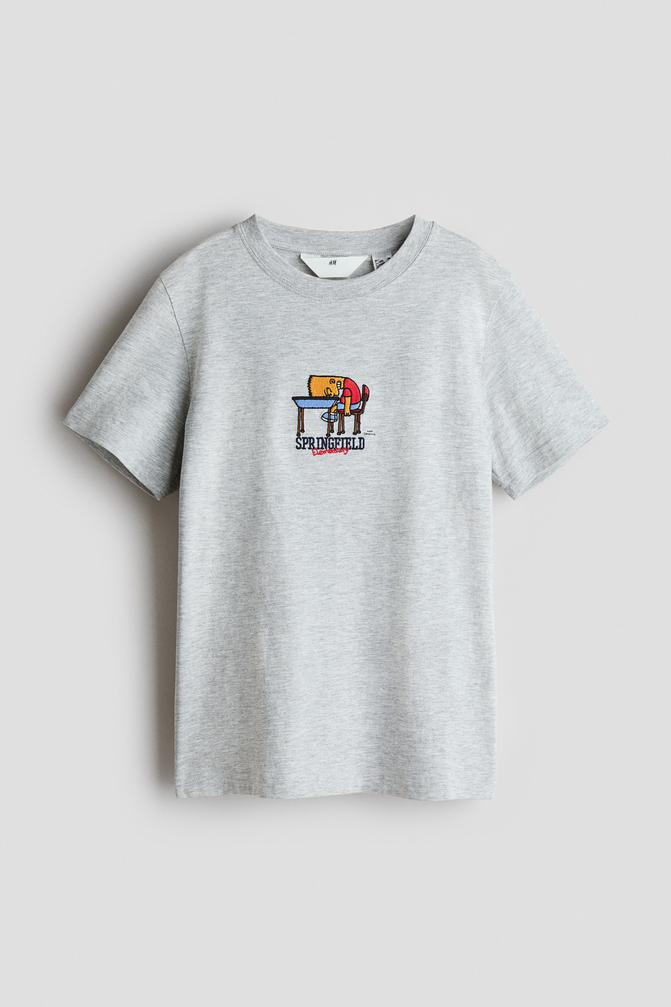 View larger image: "A heather grey T-shirt crafted from soft, printed cotton jersey is pictured from the front, showcasing a round, ribbed neckline and relaxed, dropped shoulders. The front boasts a vibrant graphic print of a cartoon character napping on a desk, with the word 'SPRINGFIELD' displayed beneath."