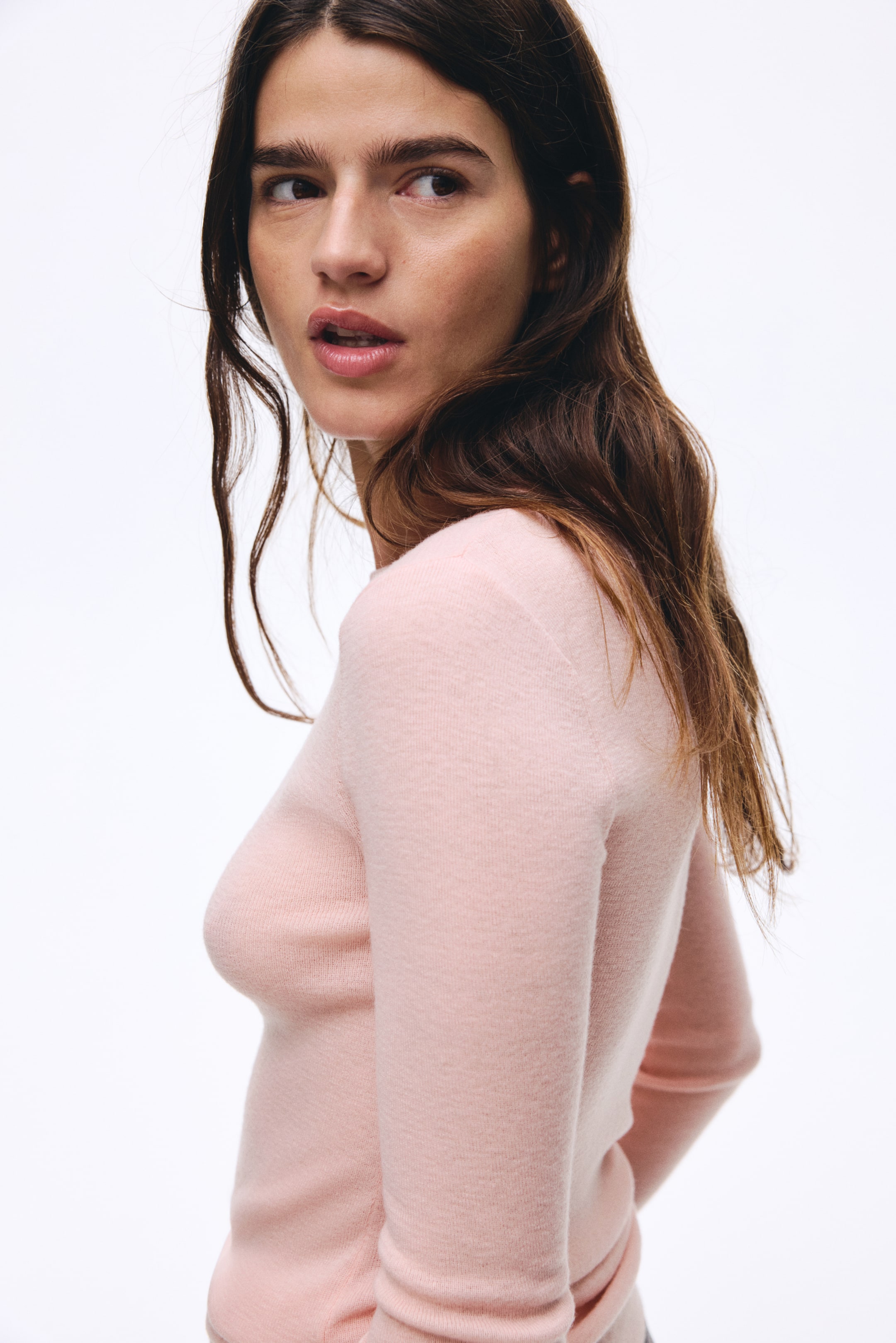 Agrandir l'image: Un haut à manches longues en maille fine de couleur rose clair est présenté de profil arrière, montrant comment il s'adapte parfaitement au corps et au bras.